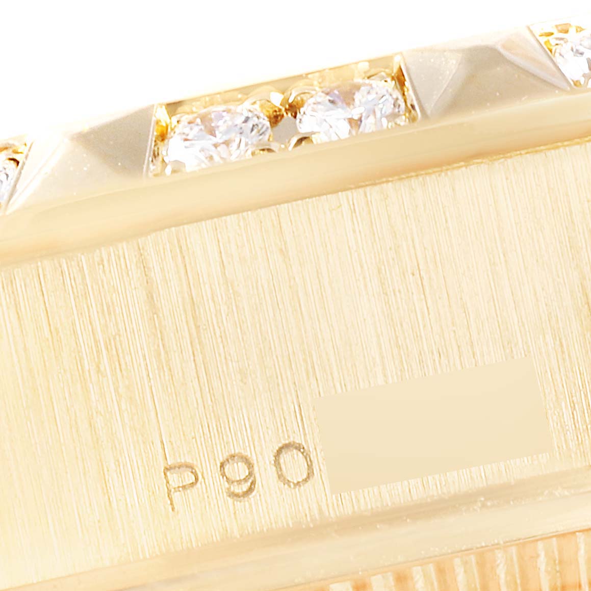This close-up image shows the side of the bezel and case of a Rolex President 79258 Women's Yellow Gold Beige Dial 79258 Women's Yellow Gold Beige Dial model, featuring diamonds and an engraved code.