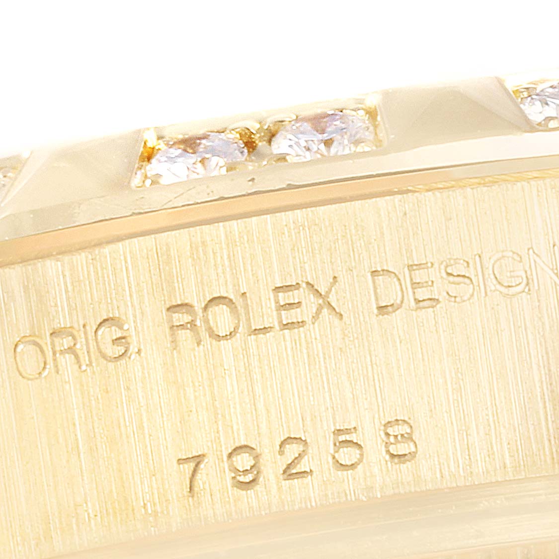 The image shows a close-up of the side of a Rolex President 79258 Women's Yellow Gold Beige Dial 79258 Women's Yellow Gold Beige Dial model watch, showcasing part of the bezel and the engraved design information.