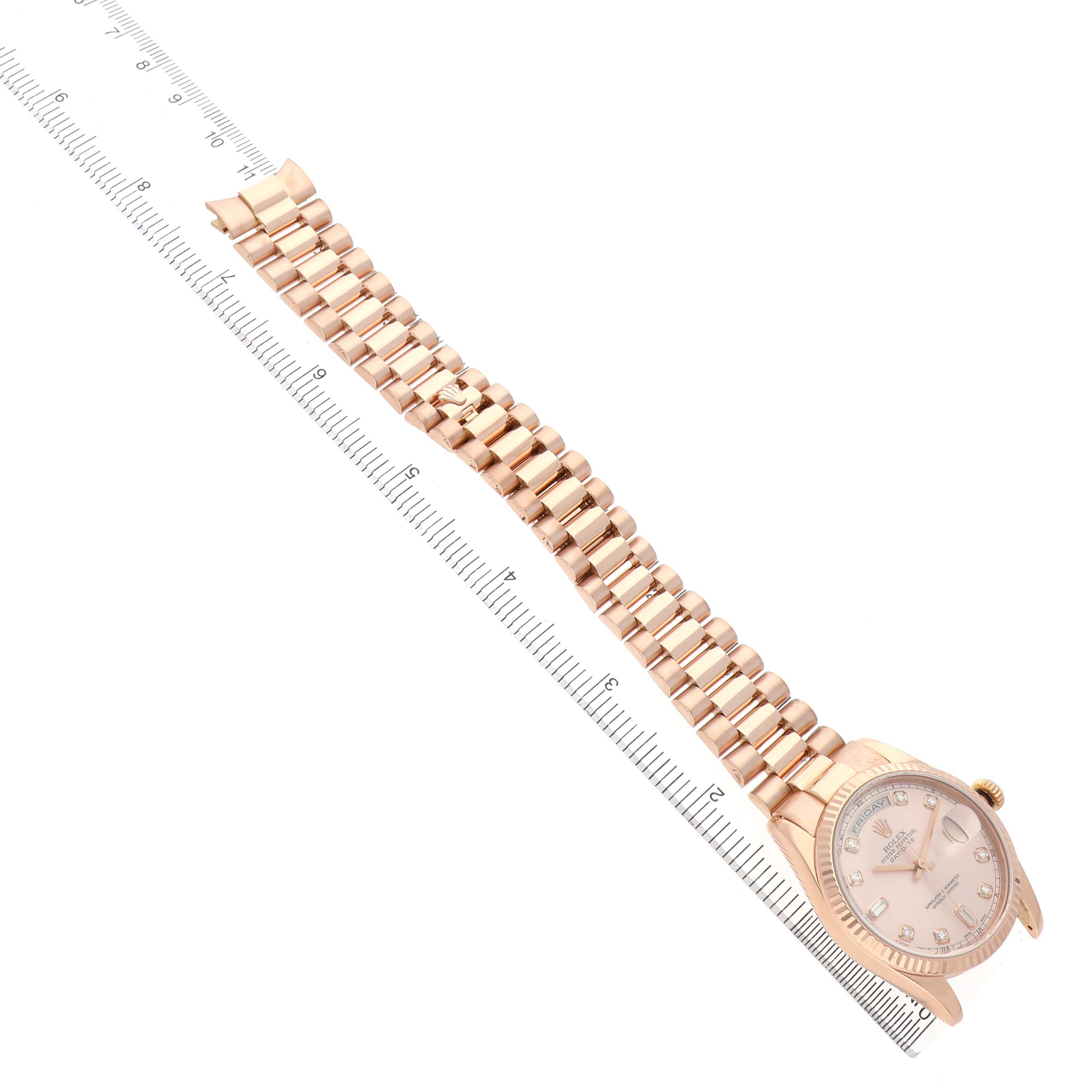 The Rolex President 118235 Men's Rose Gold Pink Dial model watch is shown from an angled top view, highlighting the face and full bracelet beside a ruler.
