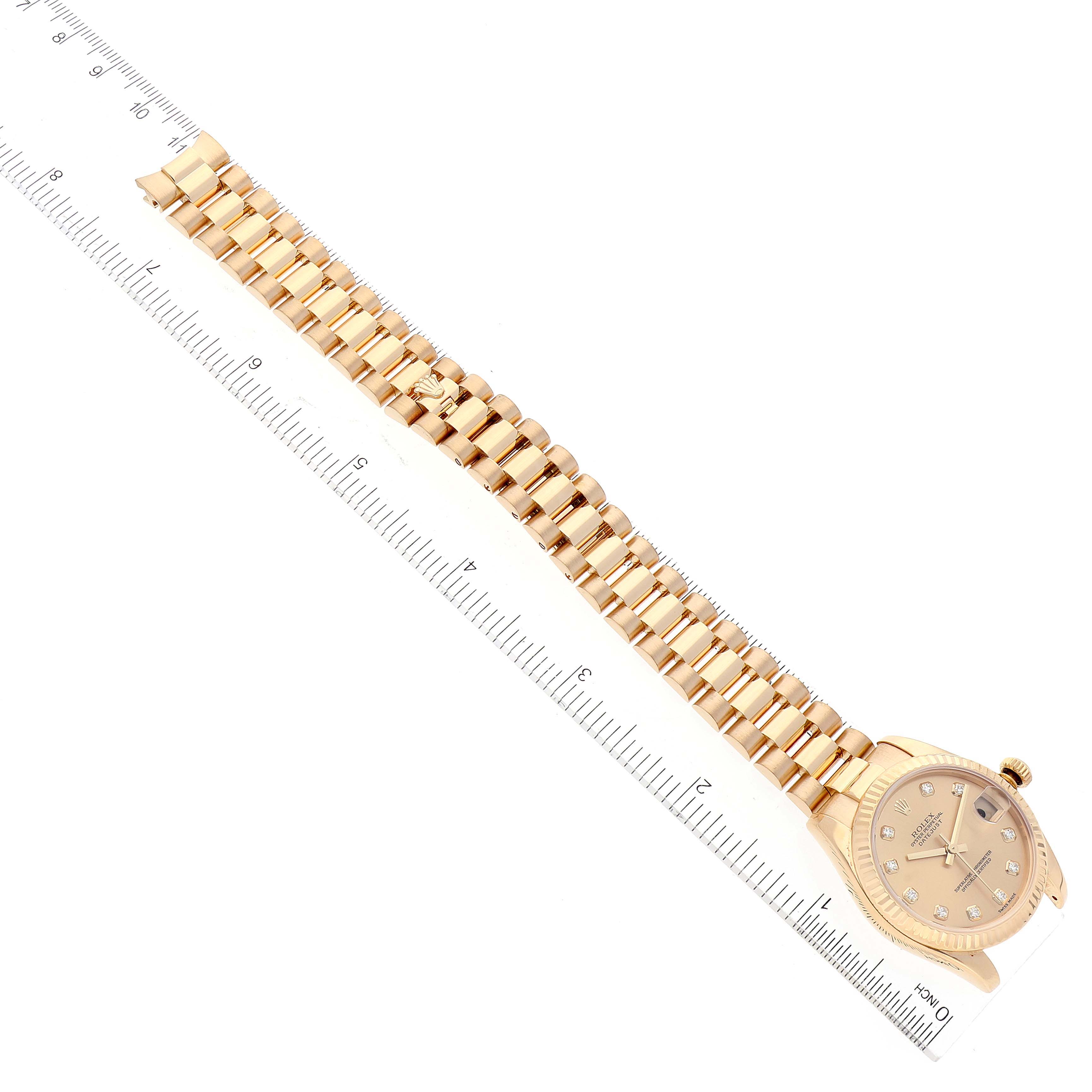 The image shows a Rolex President 178278 Women's Yellow Gold Champagne Dial 178278 Women's Yellow Gold Champagne Dial model watch laid flat with its band extended and measures beside a ruler.