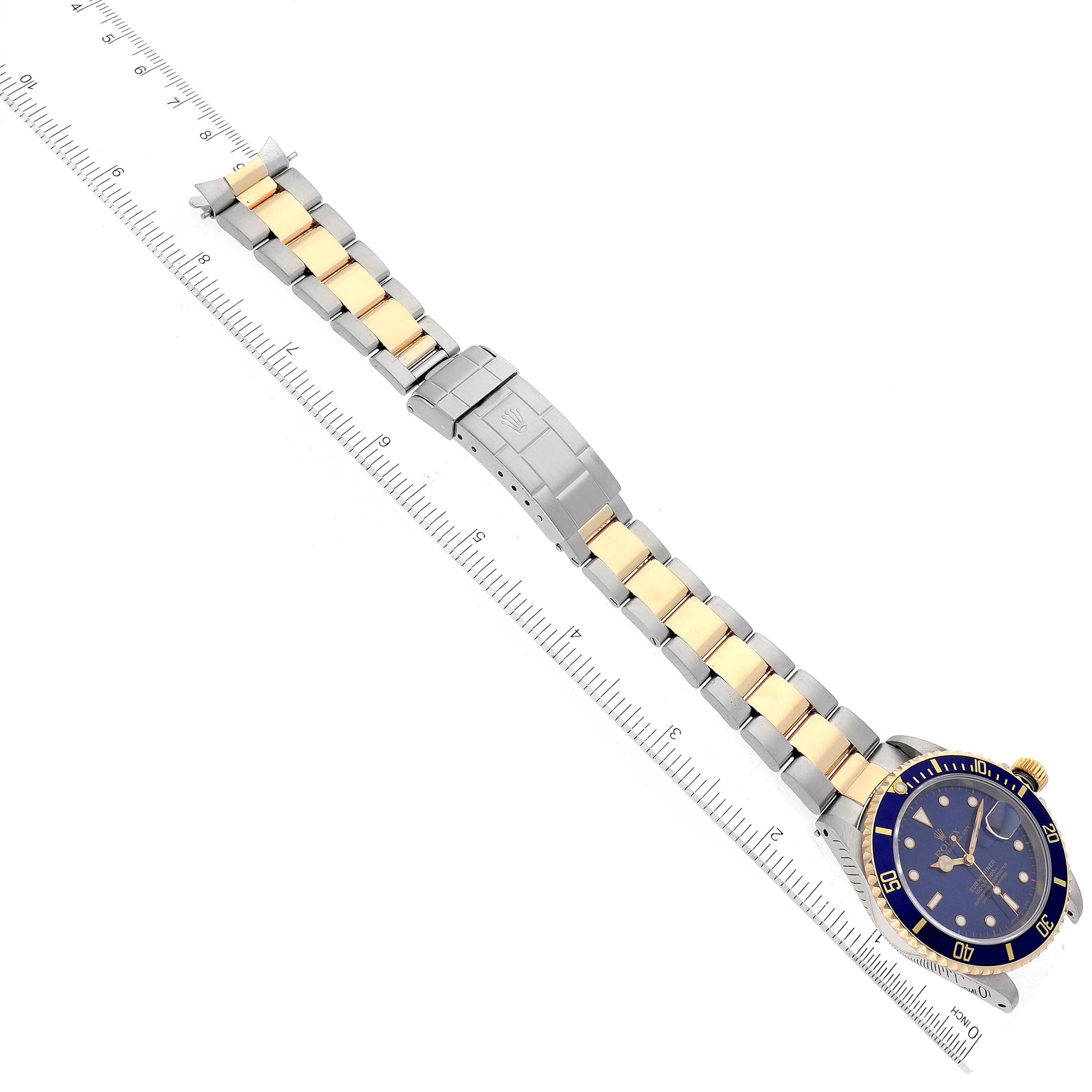 The image shows a top-down view of a Rolex Submariner 16613 Men's Steel and Gold (two tone) Blue Dial 16613 Men's Steel and Gold (two tone) Blue Dial watch with its full band and a ruler for scale.