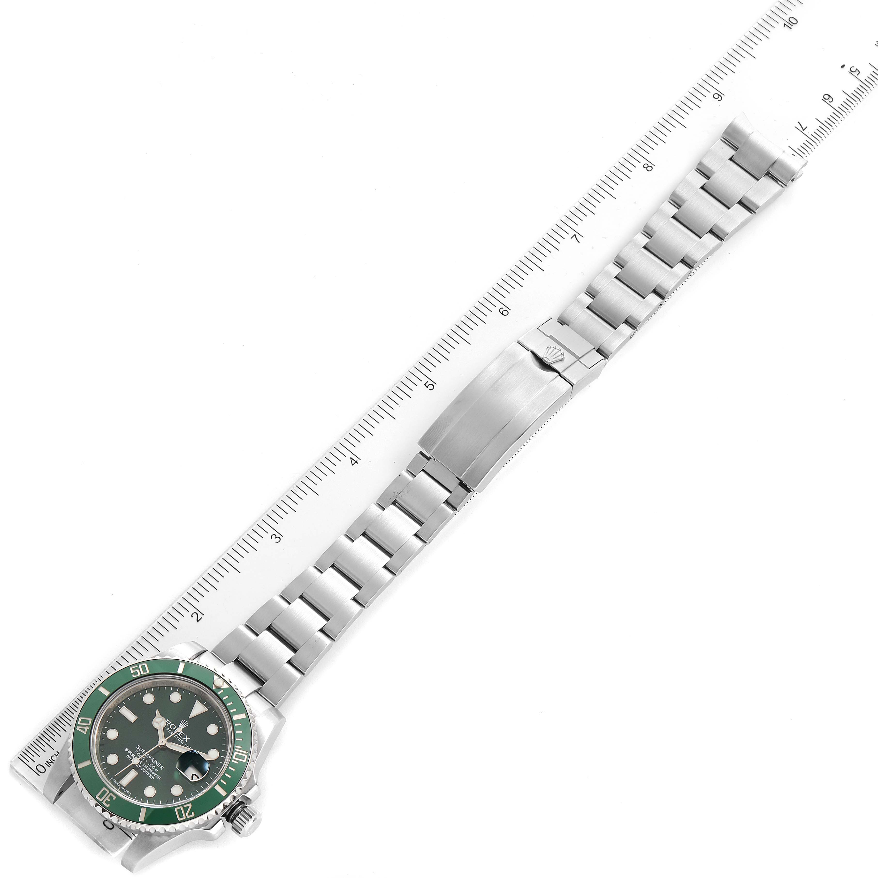 The image shows a Rolex Submariner 116610LV Men
s Stainless Steel Green Dial 116610LV Men
s Stainless Steel Green Dial watch with a green bezel and dial, laid flat alongside a ruler for measurement.