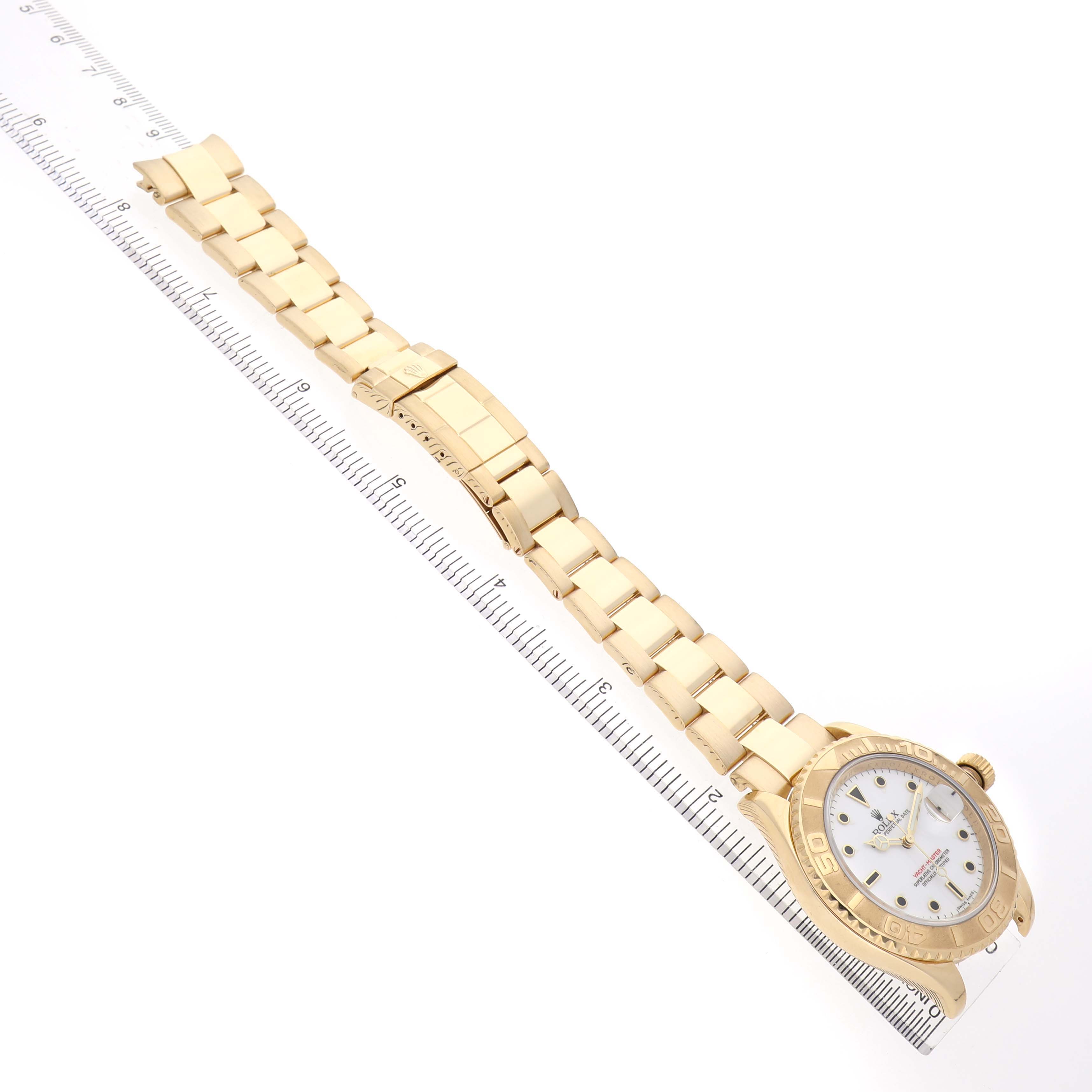 The Rolex Yacht-Master 16628 Men's Yellow Gold White Dial watch is shown from an overhead angle, displaying the face, case, and full bracelet with a measuring ruler.