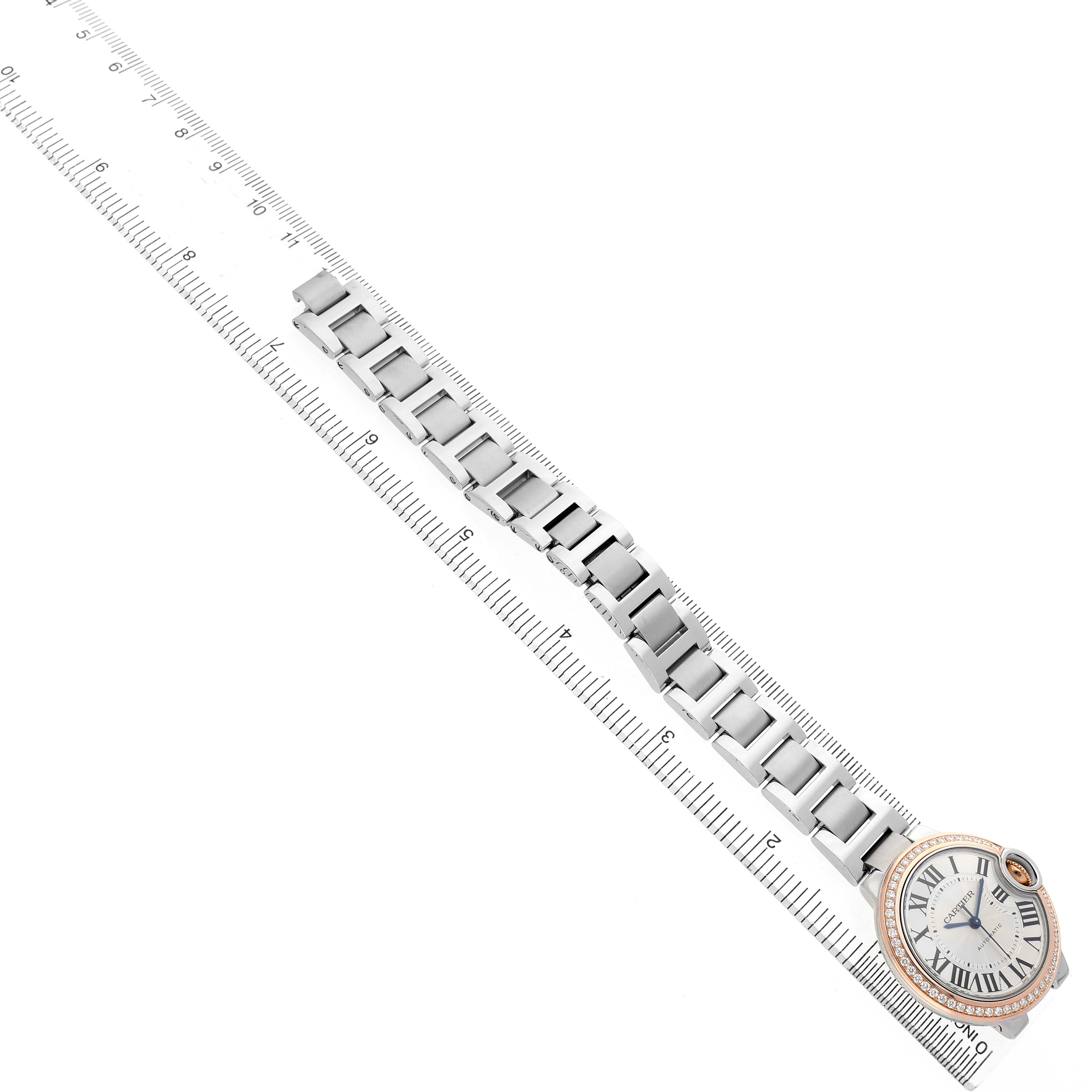 The Ballon Bleu by Cartier is shown at an angle highlighting its watch face and metal bracelet against a ruler backdrop.