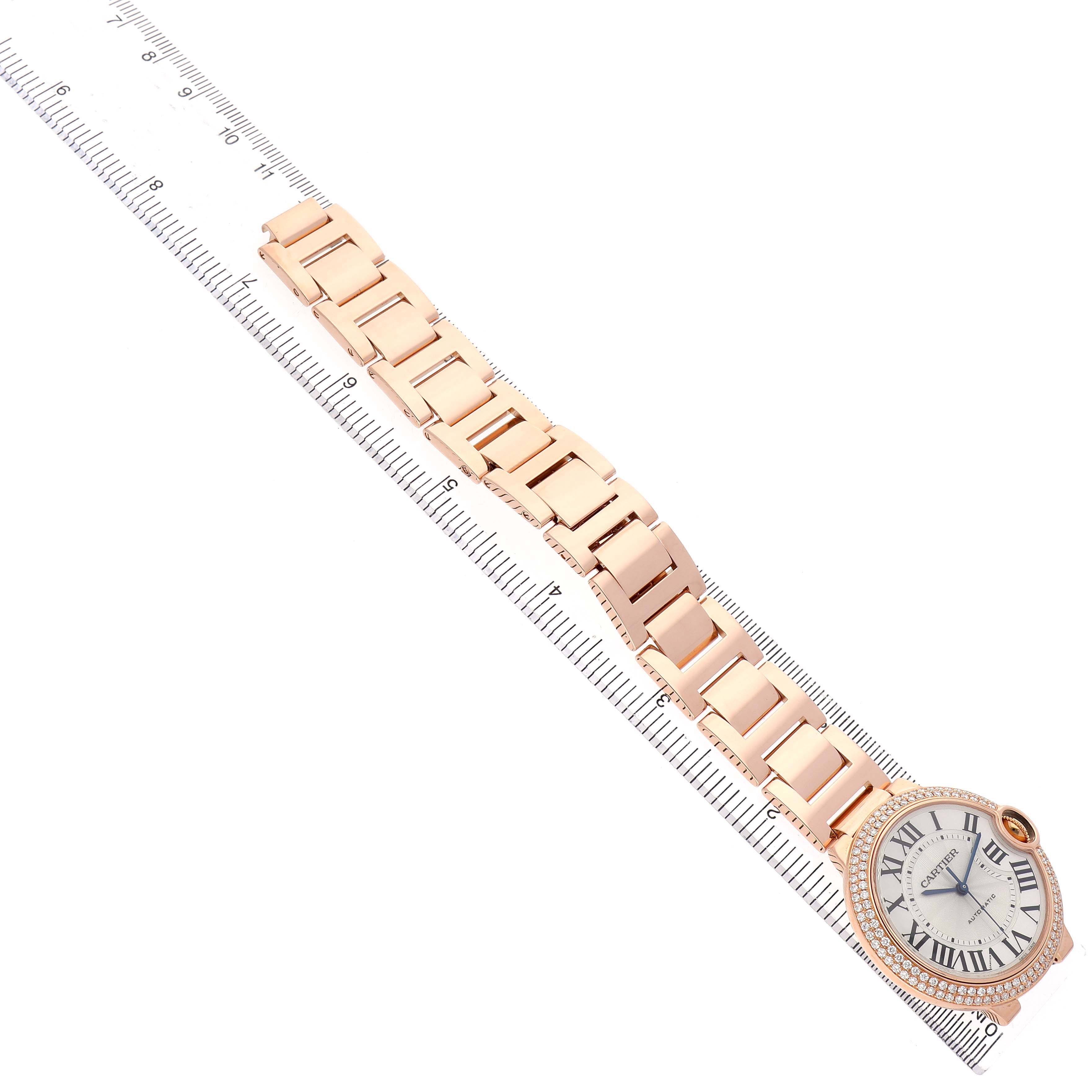 The Cartier Ballon Bleu WE9005Z3 Women's Rose Gold Silver Dial watch is shown from a top-down angle, highlighting the face and bracelet alongside a ruler for scale.