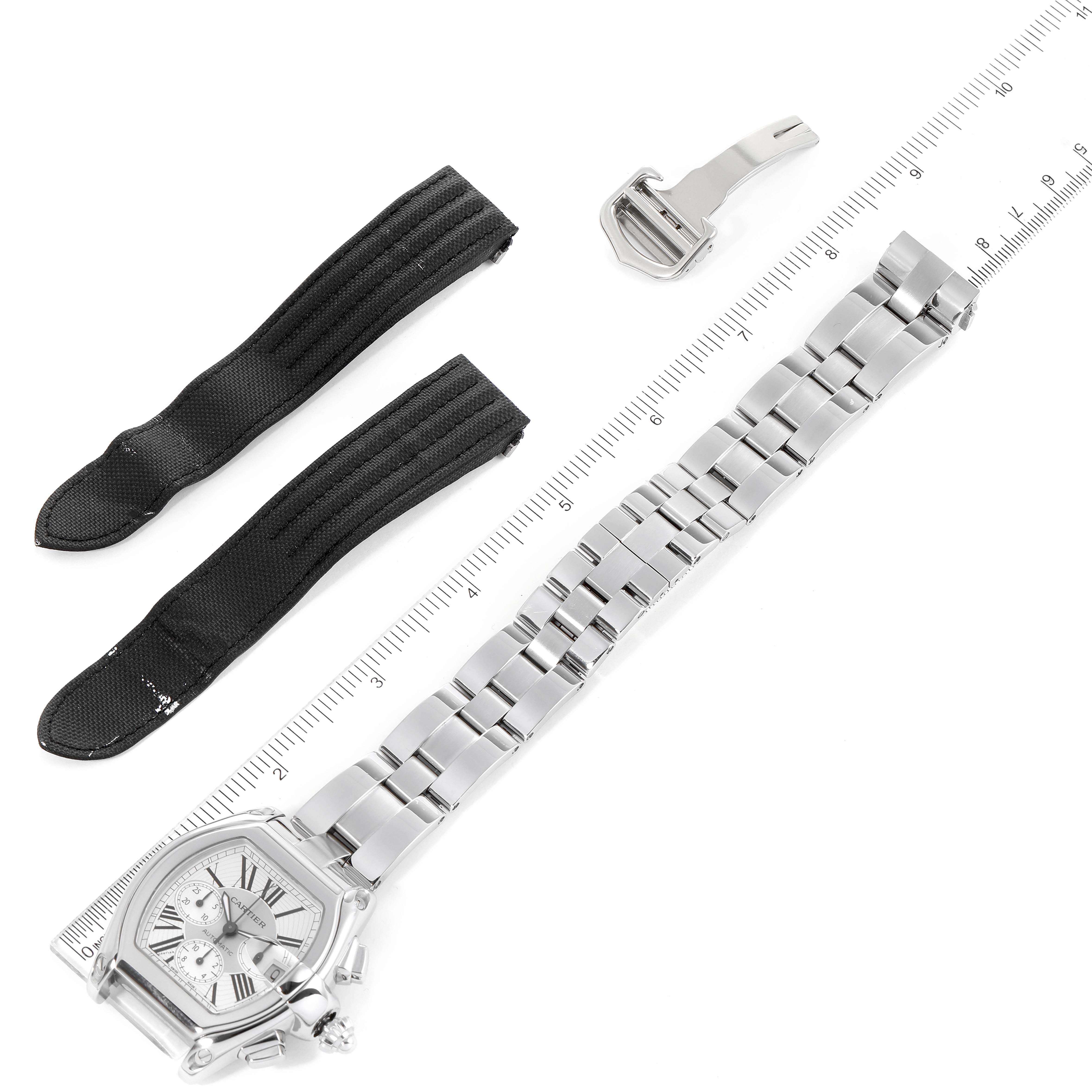This image shows a Cartier Roadster W62019X6 Men
s Stainless Steel Silver Dial W62019X6 Men
s Stainless Steel Silver Dial watch with its stainless steel band, two black fabric straps, and a buckle, laid flat above a ruler.
