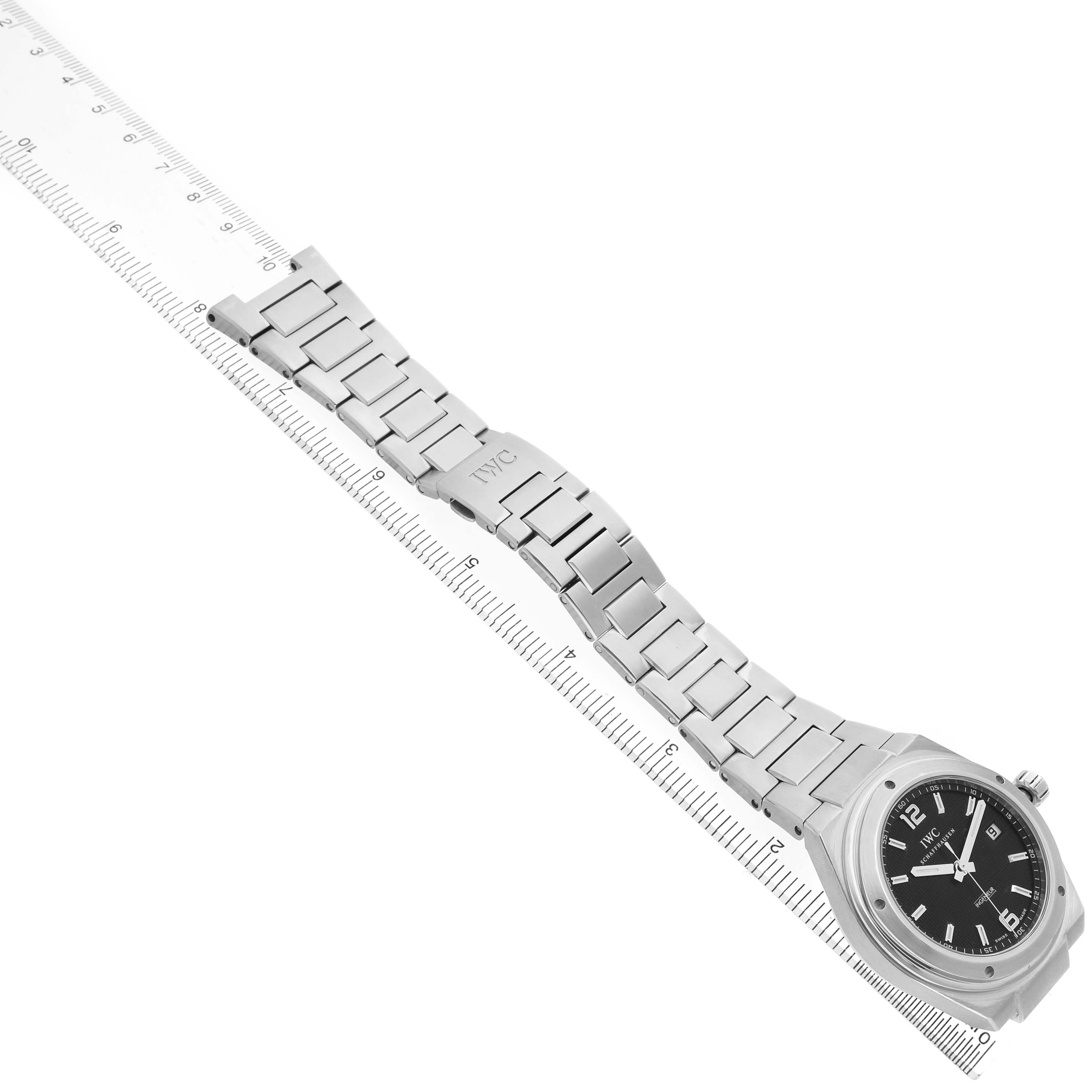 The IWC Ingenieur IW322701 Men's Stainless Steel Black Dial watch is shown at an angled top-down view, highlighting its metal bracelet and clasp alongside a ruler for scale.
