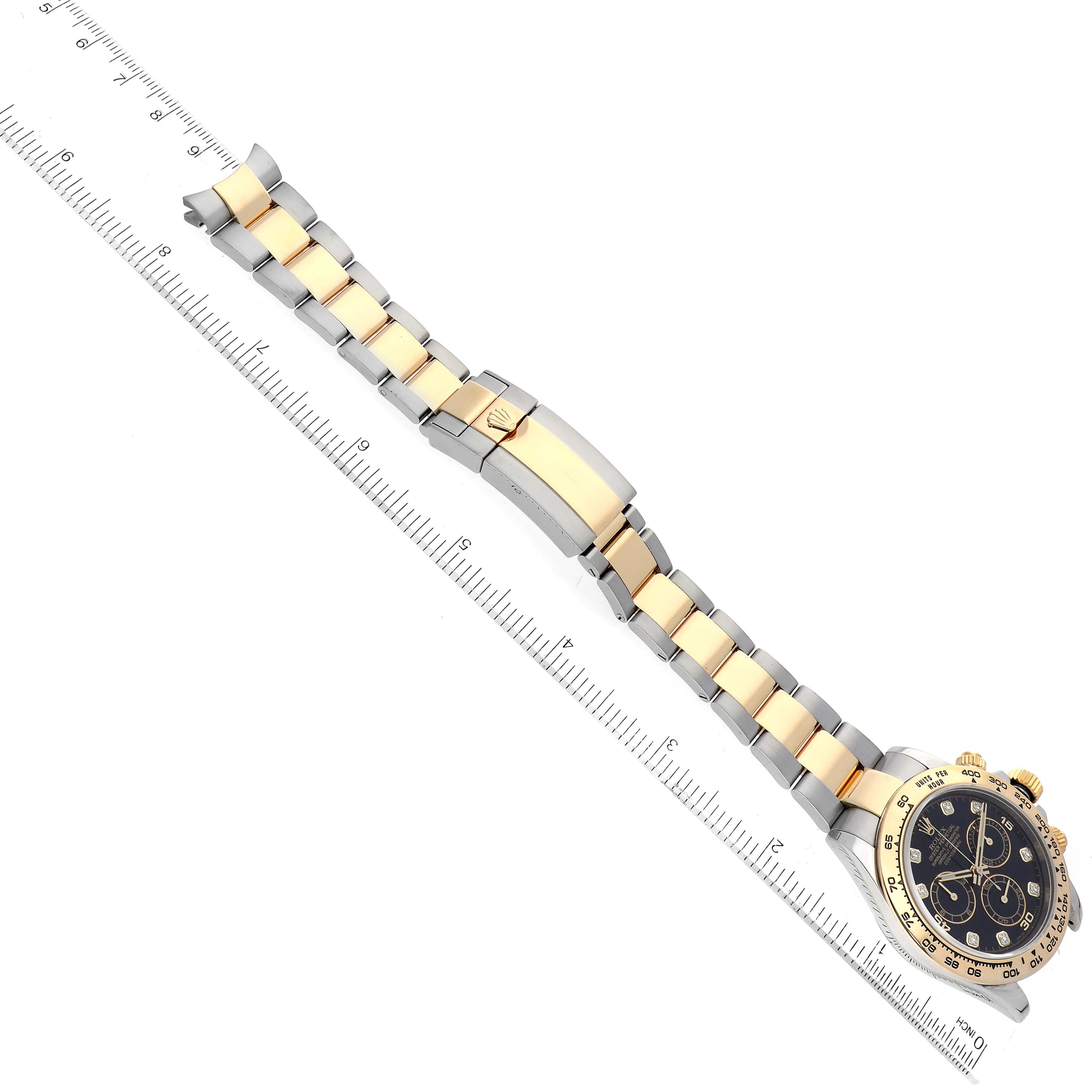 The image shows a Rolex Daytona 116503 Men
s Steel and Gold (two tone) Black Dial 116503 Men
s Steel and Gold (two tone) Black Dial watch laid flat with its gold and silver bracelet fully extended alongside a ruler.