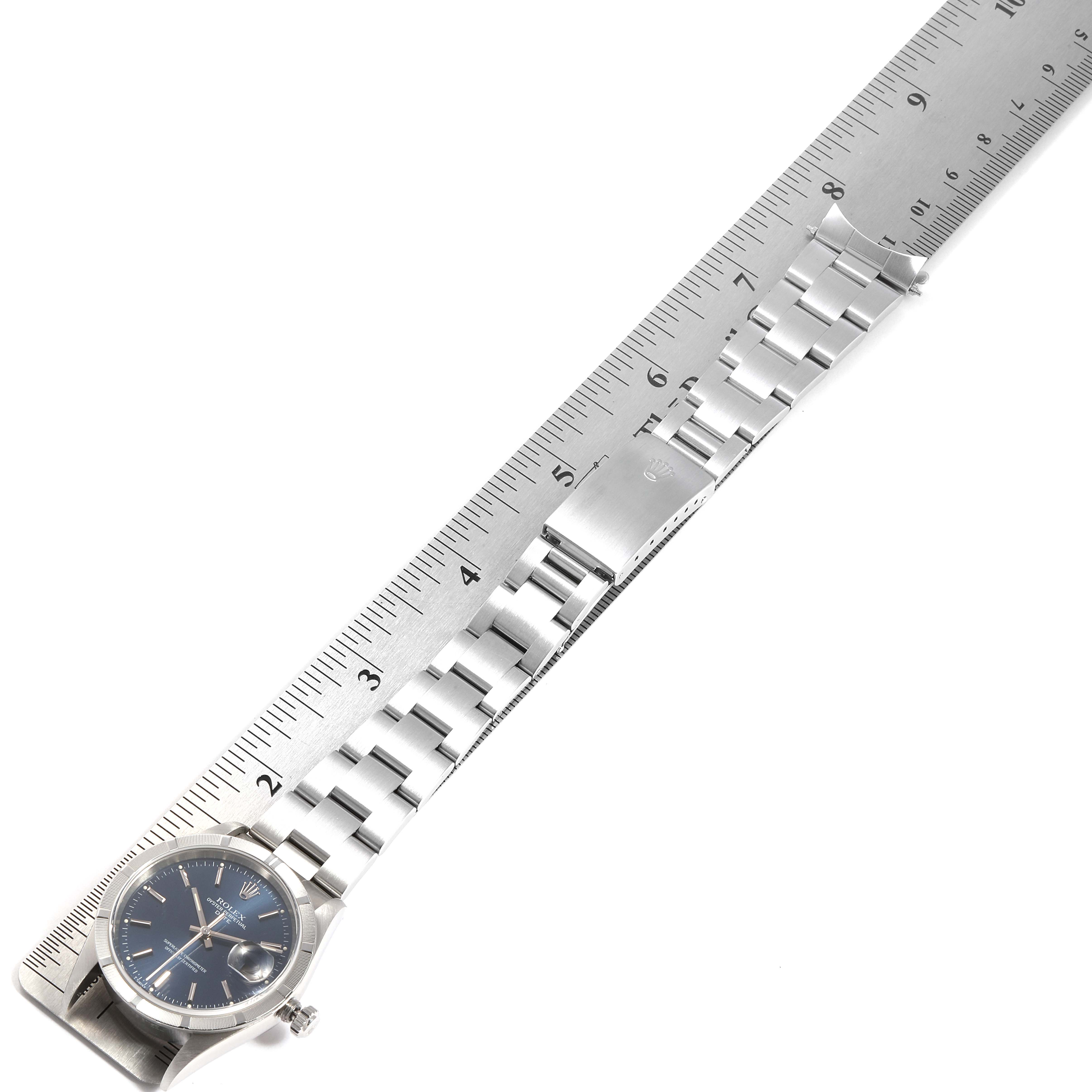 The image shows a Rolex Date 15210 Men's Stainless Steel Blue Dial 15210 Men's Stainless Steel Blue Dial model watch laid flat against a ruler, displaying the watch face, band, and clasp.