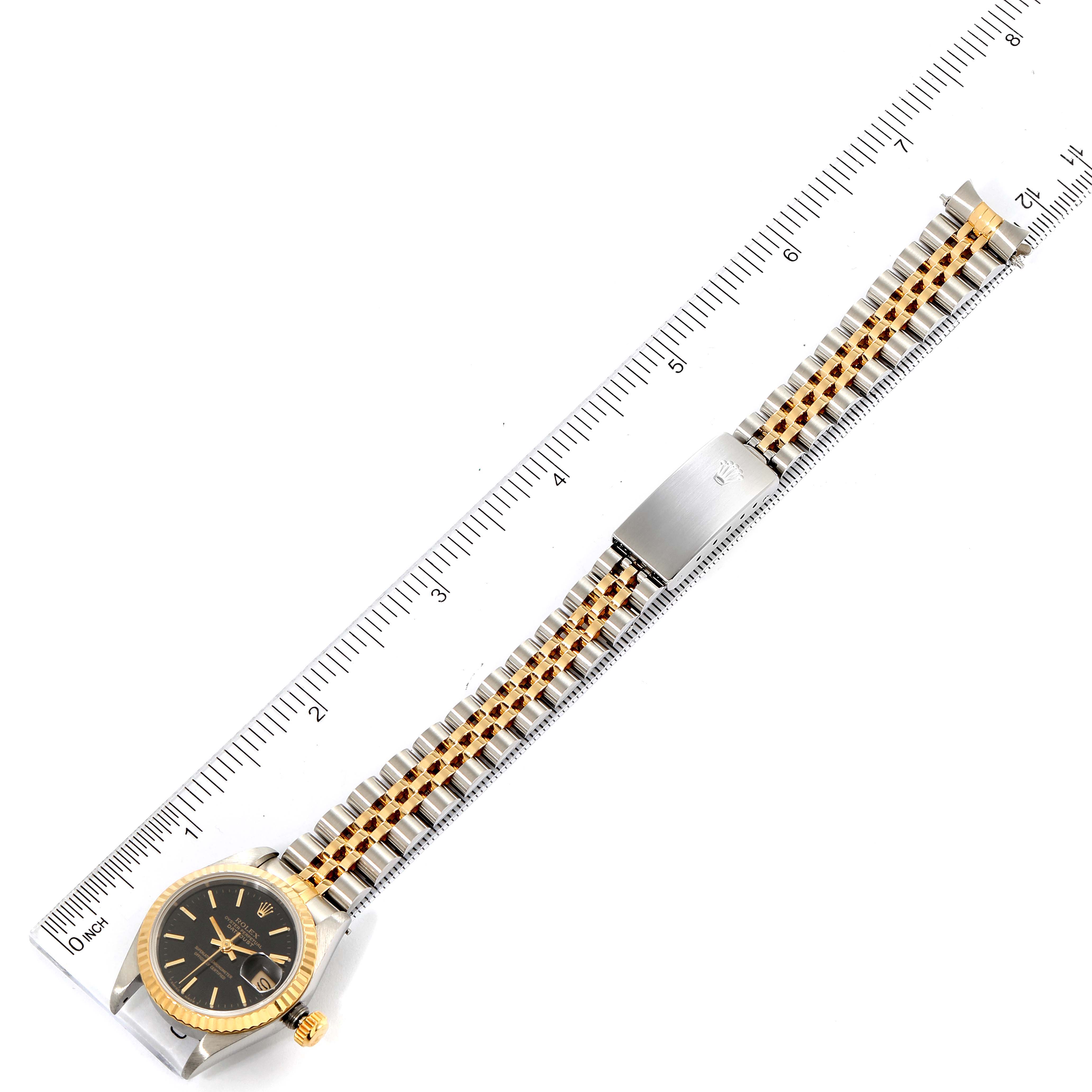 The Rolex Datejust 69173 Women
s Steel and Gold (two tone) Black Dial 69173 Women
s Steel and Gold (two tone) Black Dial is shown from above, displaying the watch face, gold bezel, Jubilee bracelet, and clasp alongside a ruler.