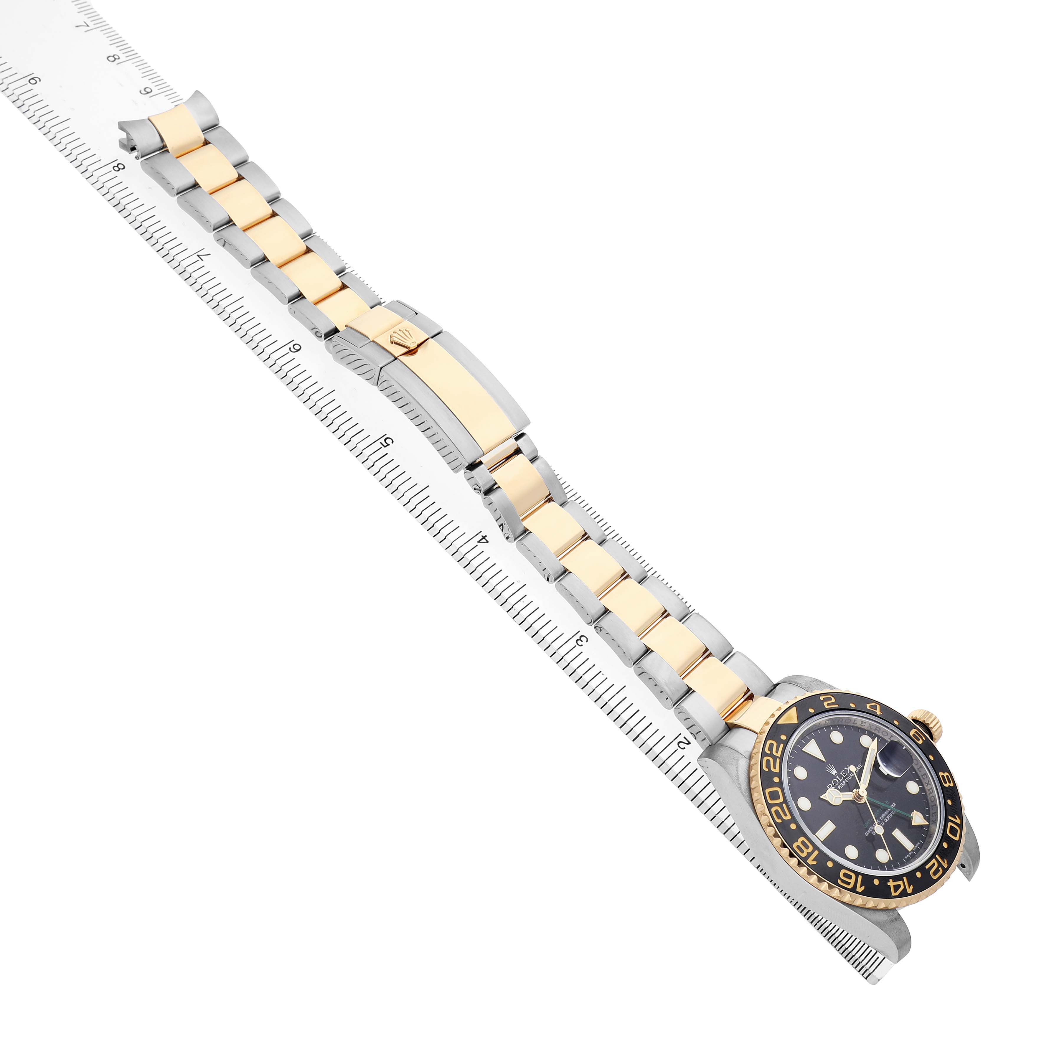 The Rolex GMT-Master 116713 Men's Steel and Gold (two tone) Black Dial watch is shown diagonally with the bracelet and face visible, positioned alongside a ruler.