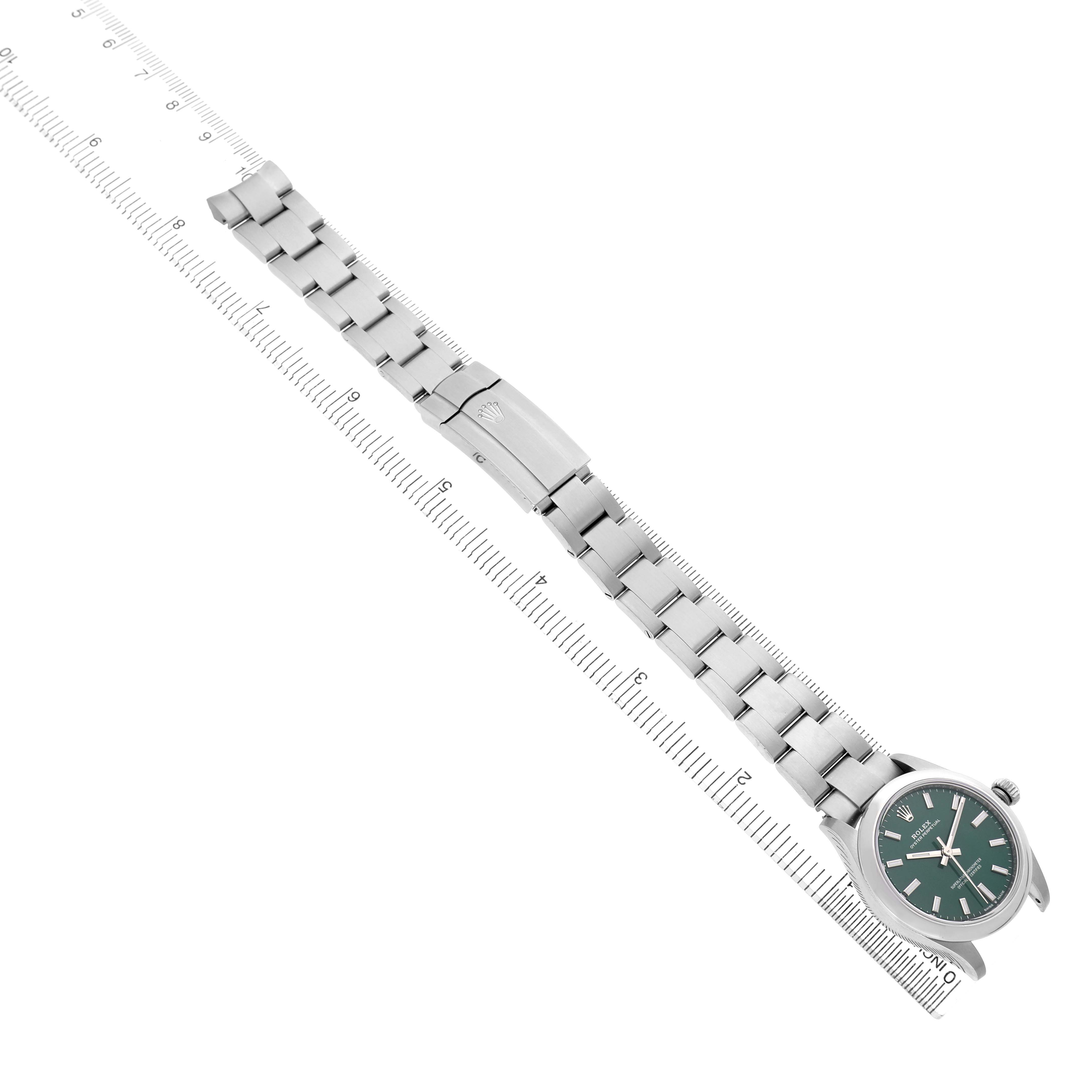 The Rolex Oyster Perpetual 277200 Women's Stainless Steel Green Dial watch is displayed flat, showing the face, bracelet, and clasp diagonally across a ruler.