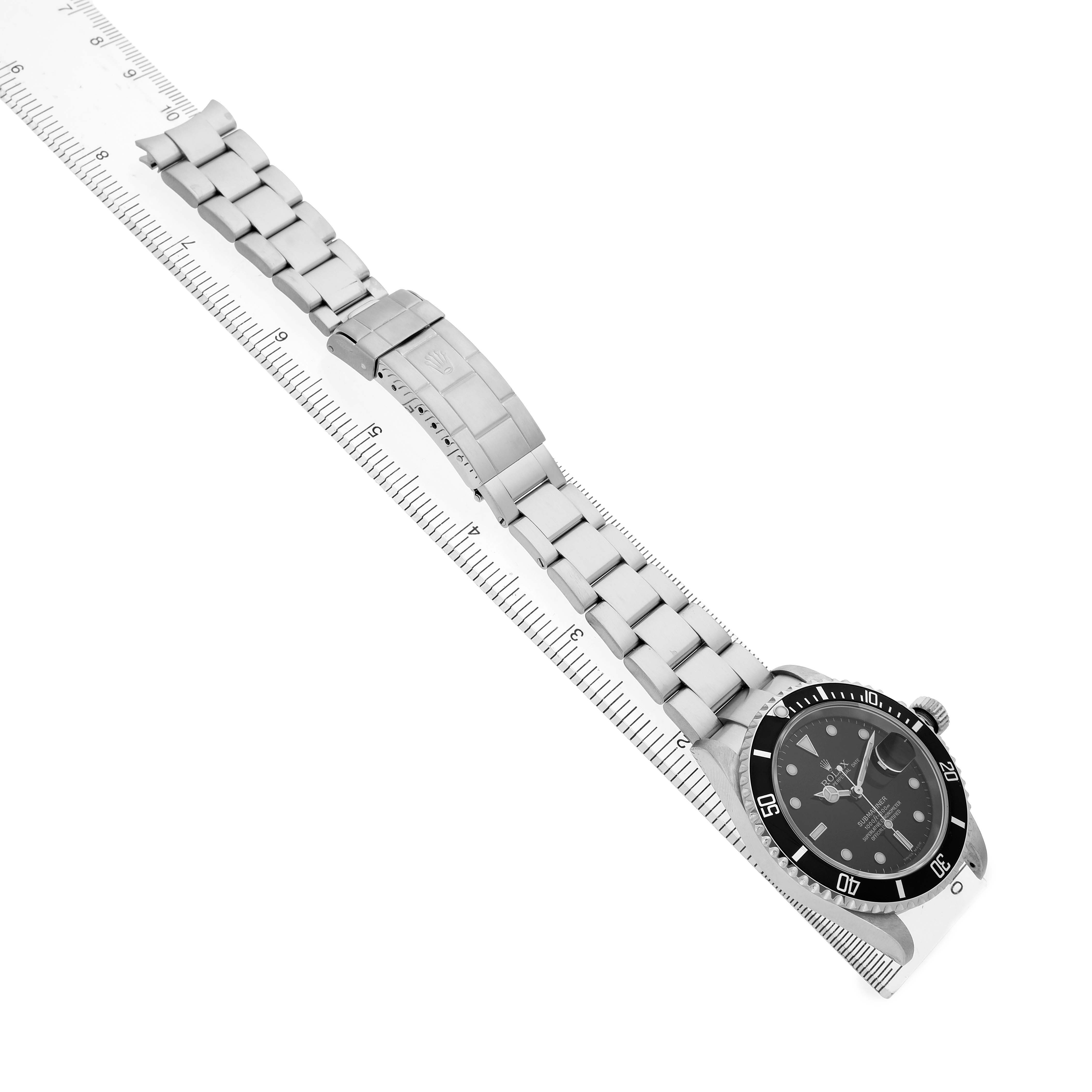 The image shows a top-down angle of a Rolex Submariner 16610 Men's Stainless Steel Black Dial, featuring its full bracelet, clasp, and dial resting on a ruler.