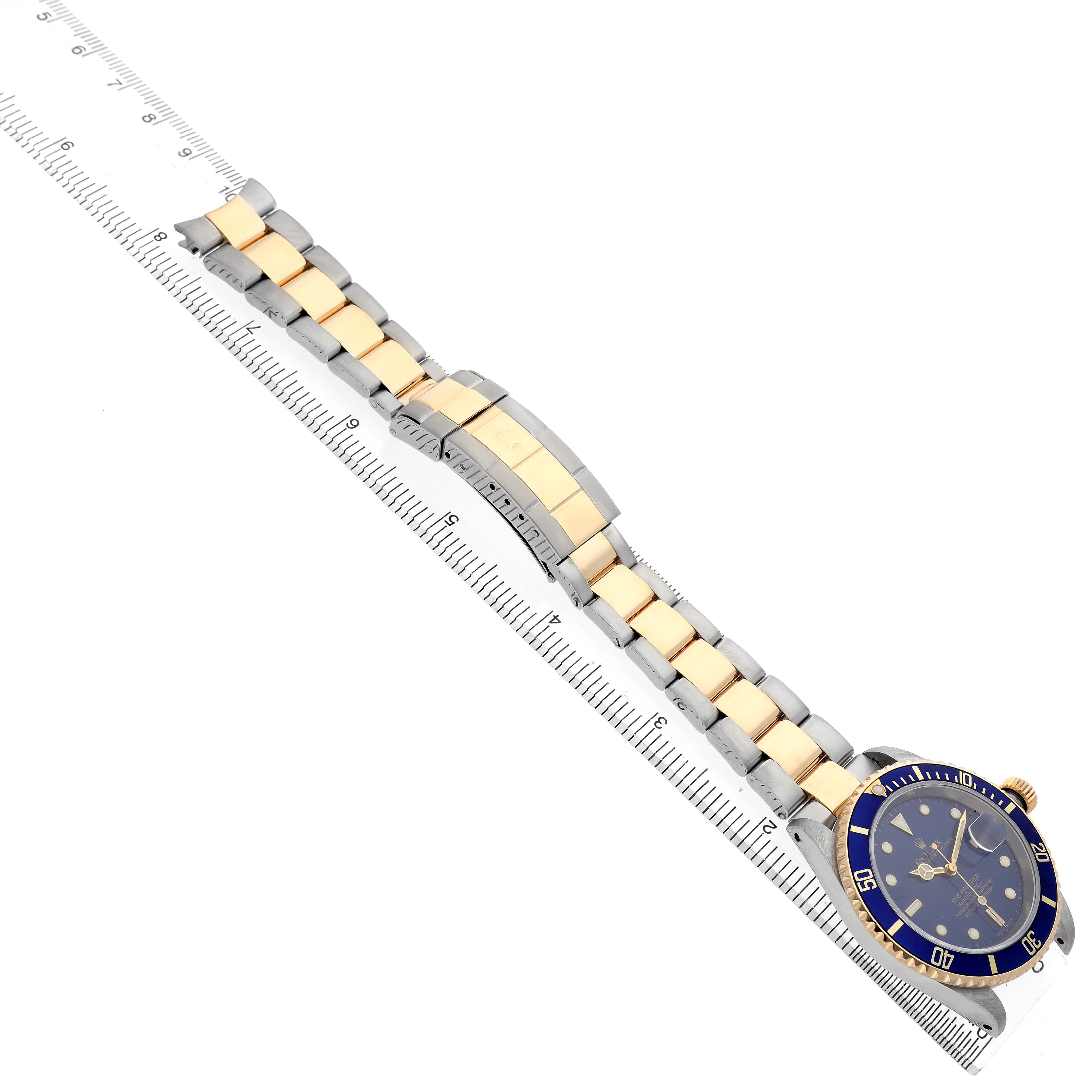 The image shows a Rolex Submariner 16613 Men's Steel and Gold (two tone) Blue Dial laid diagonally, with focus on its bracelet, clasp, and partially visible watch face.
