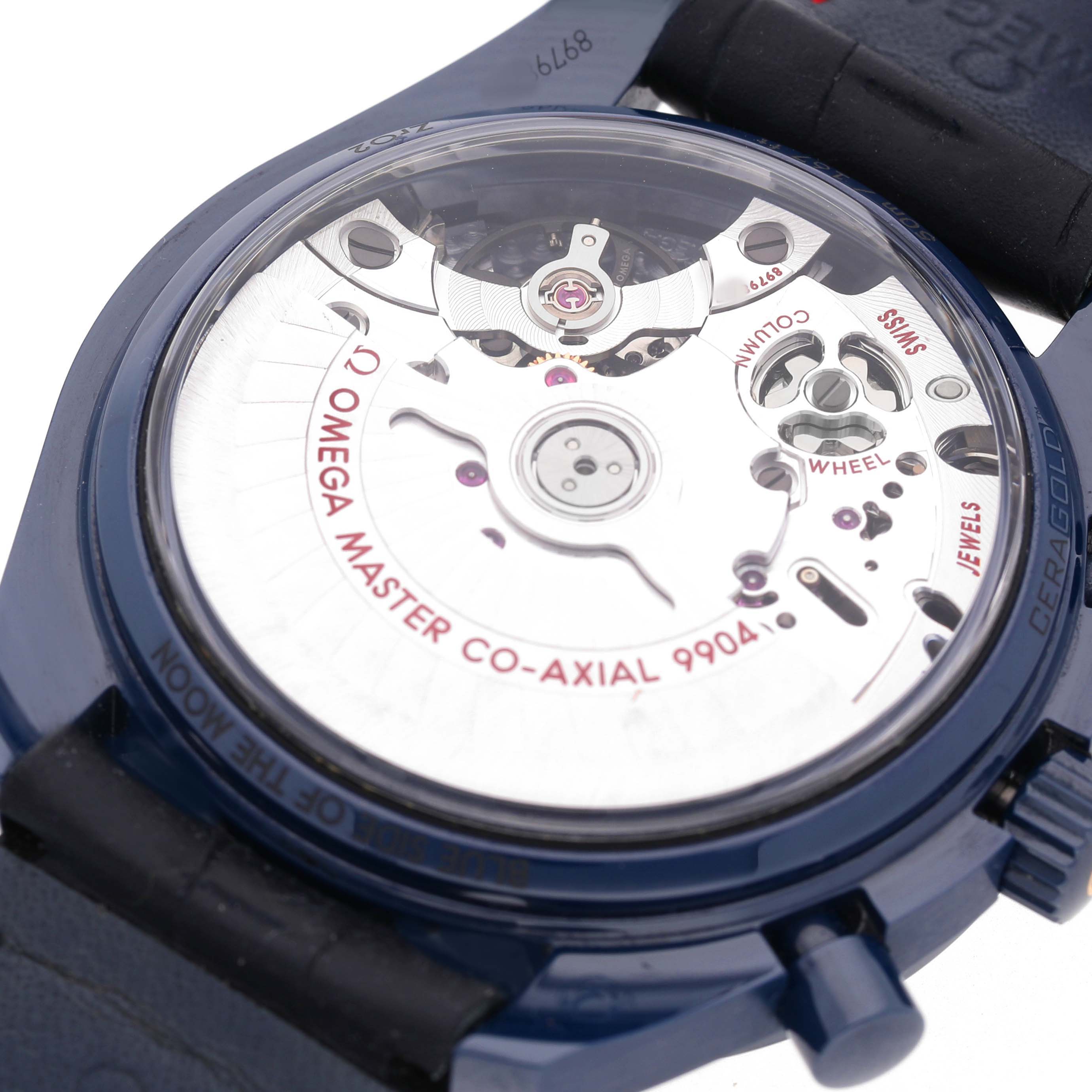 The image shows the back view of an Omega Speedmaster 304.93.44.52.03.002 Men's Ceramic Blue Dial watch, highlighting the Master Co-Axial 9904 movement and intricate inner mechanics.