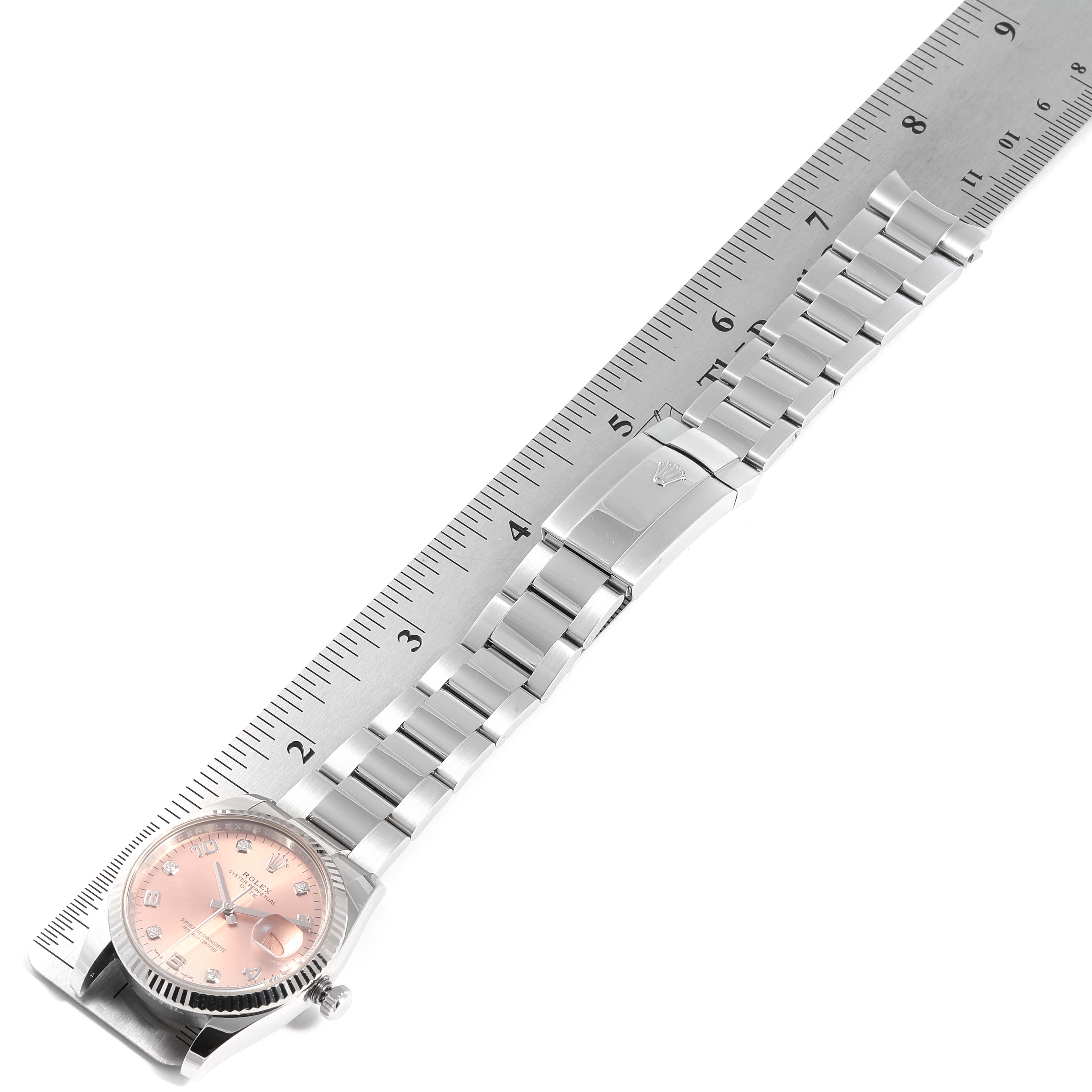 The image shows a side angle of a Rolex Datejust 115234 Men's Stainless Steel Pink Dial 115234 Men's Stainless Steel Pink Dial watch, highlighting the dial, bezel, bracelet, and clasp beside a ruler.