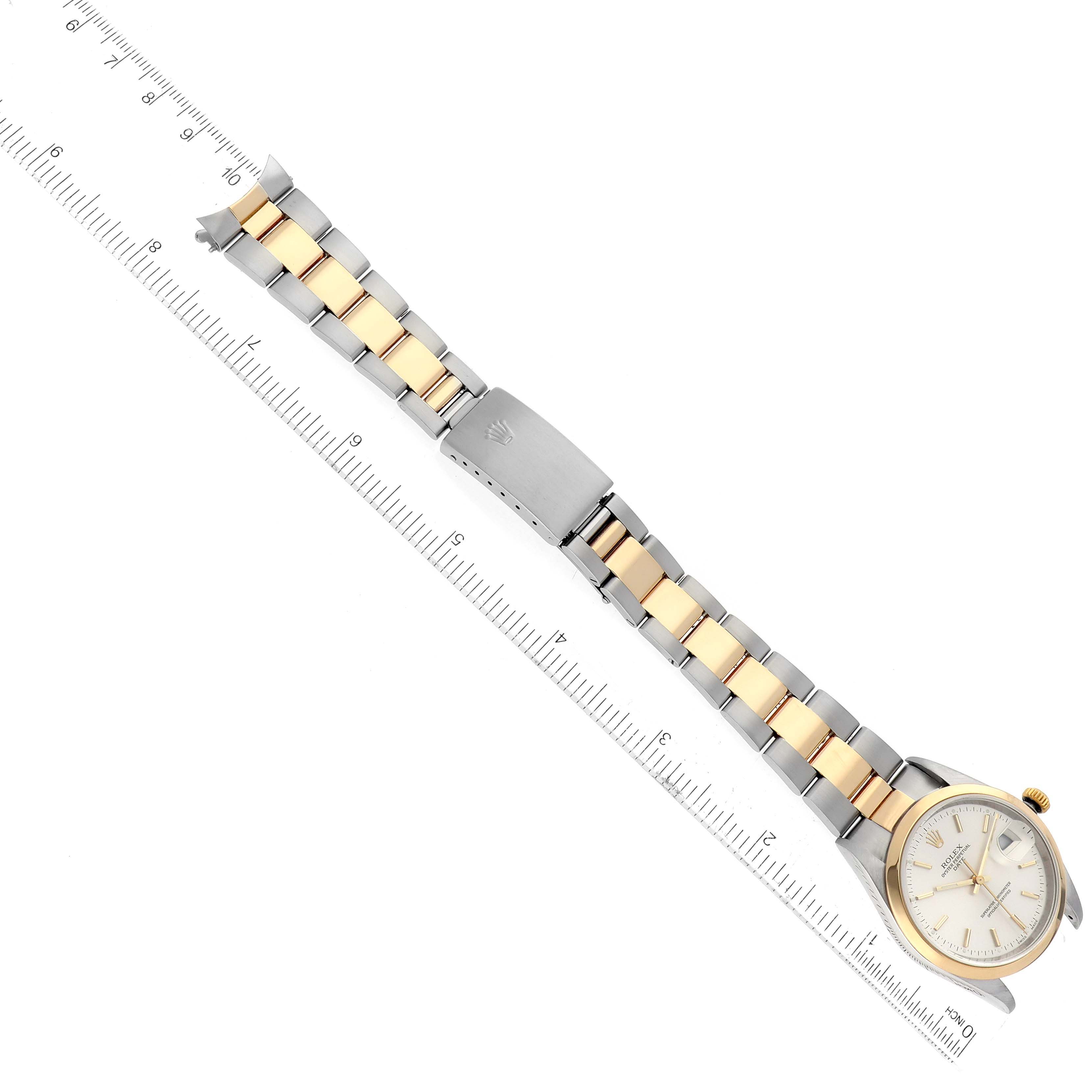The Rolex Date 15203 Men's Steel and Gold (two tone) Silver Dial 15203 Men's Steel and Gold (two tone) Silver Dial model watch is shown laid flat with its bracelet extended next to a ruler, displaying the watch face and clasp.