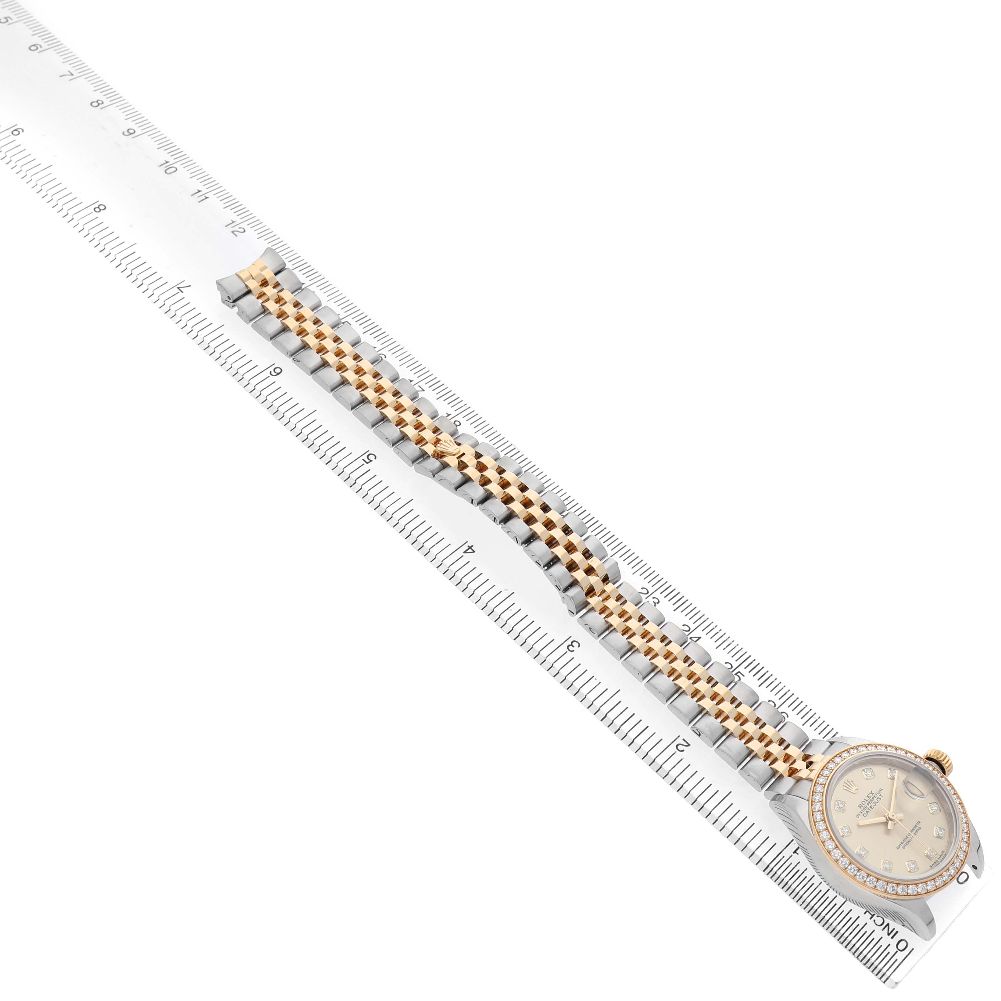 The Rolex Datejust 279383 Women's Stainless Steel Champagne Dial watch is shown from a top view, highlighting the dial and two-tone bracelet, lying alongside a ruler.