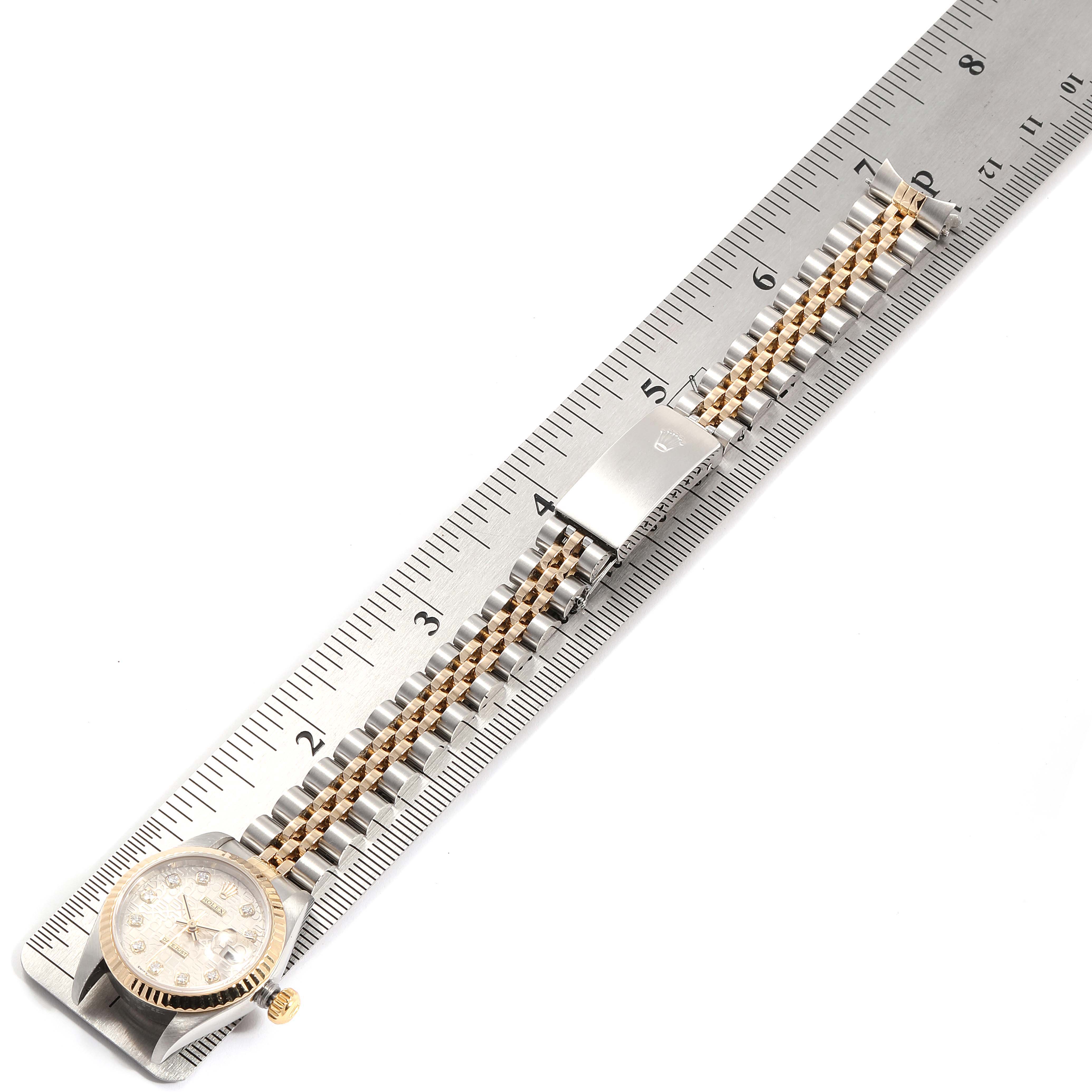The Rolex Datejust 79173 Women's Steel and Gold (two tone) Silver Dial 79173 Women's Steel and Gold (two tone) Silver Dial watch is laid flat on a ruler, showcasing its dial, case, and Jubilee bracelet.