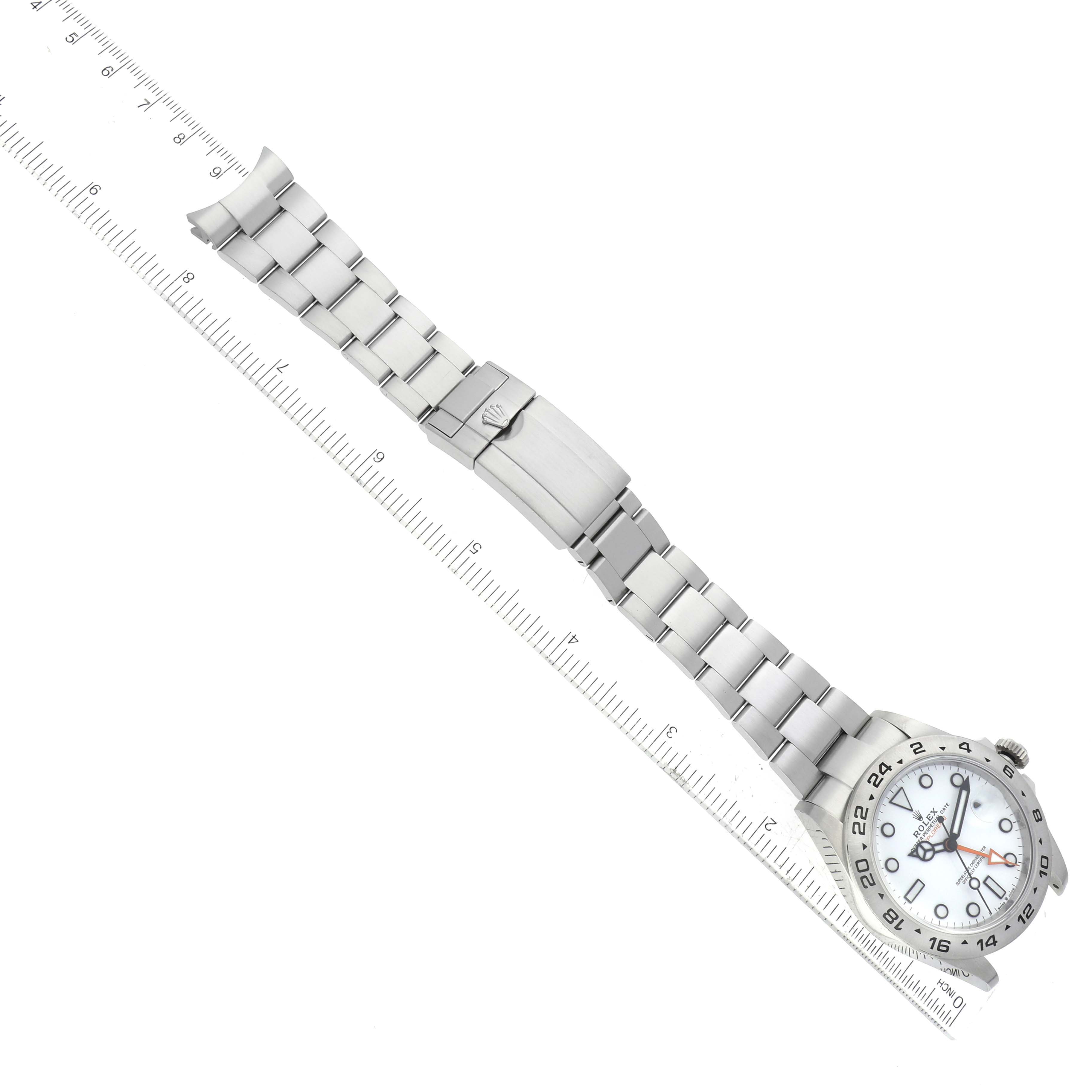 The image shows a top-down view of a Rolex Explorer 226570 Men's Stainless Steel White Dial 226570 Men's Stainless Steel White Dial watch, displaying its dial, bezel, bracelet, and clasp on a ruler for scale.