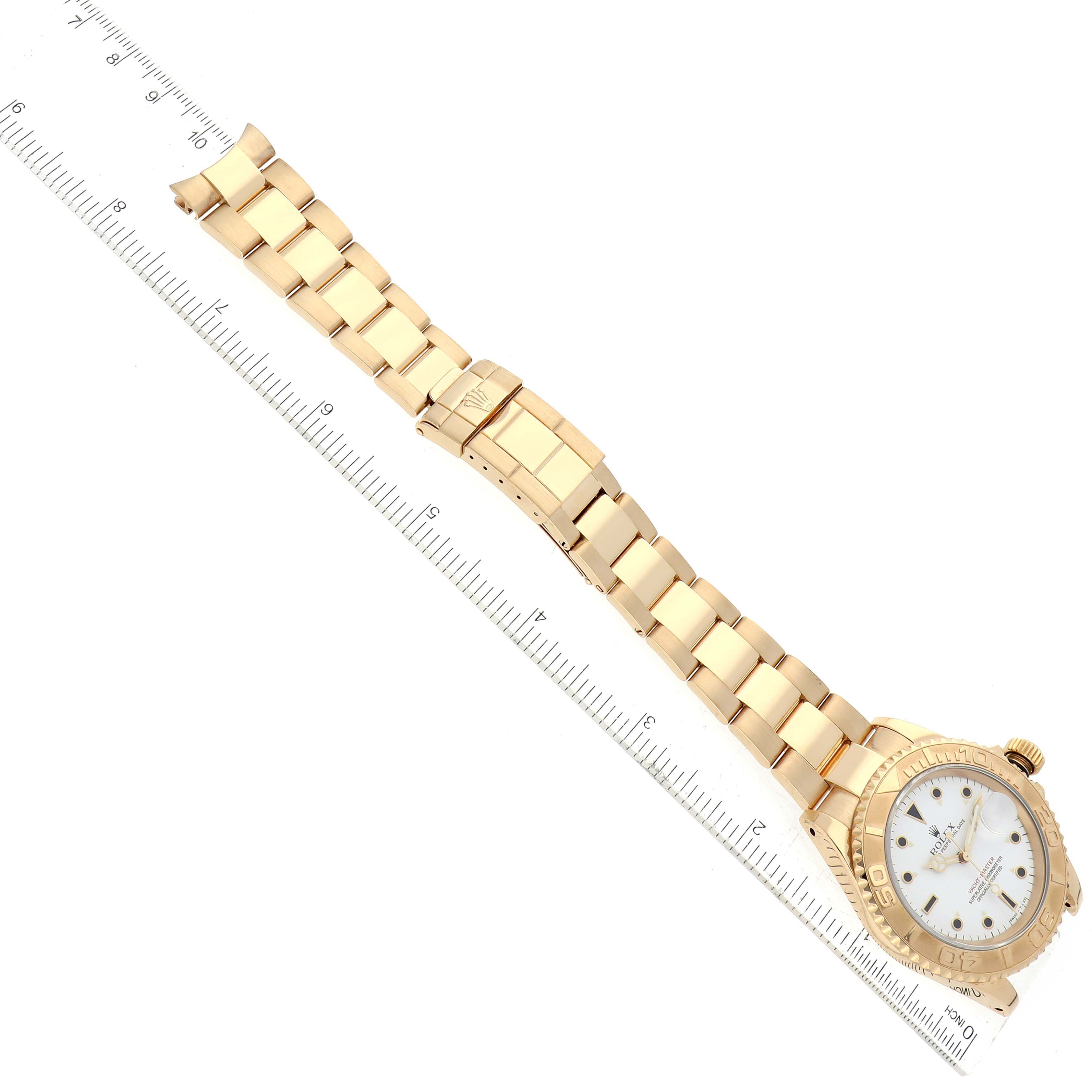 The image shows a top-down view of a Rolex Yacht-Master 16628 Men's Yellow Gold White Dial 16628 Men's Yellow Gold White Dial watch with a gold bracelet, placed next to a ruler.