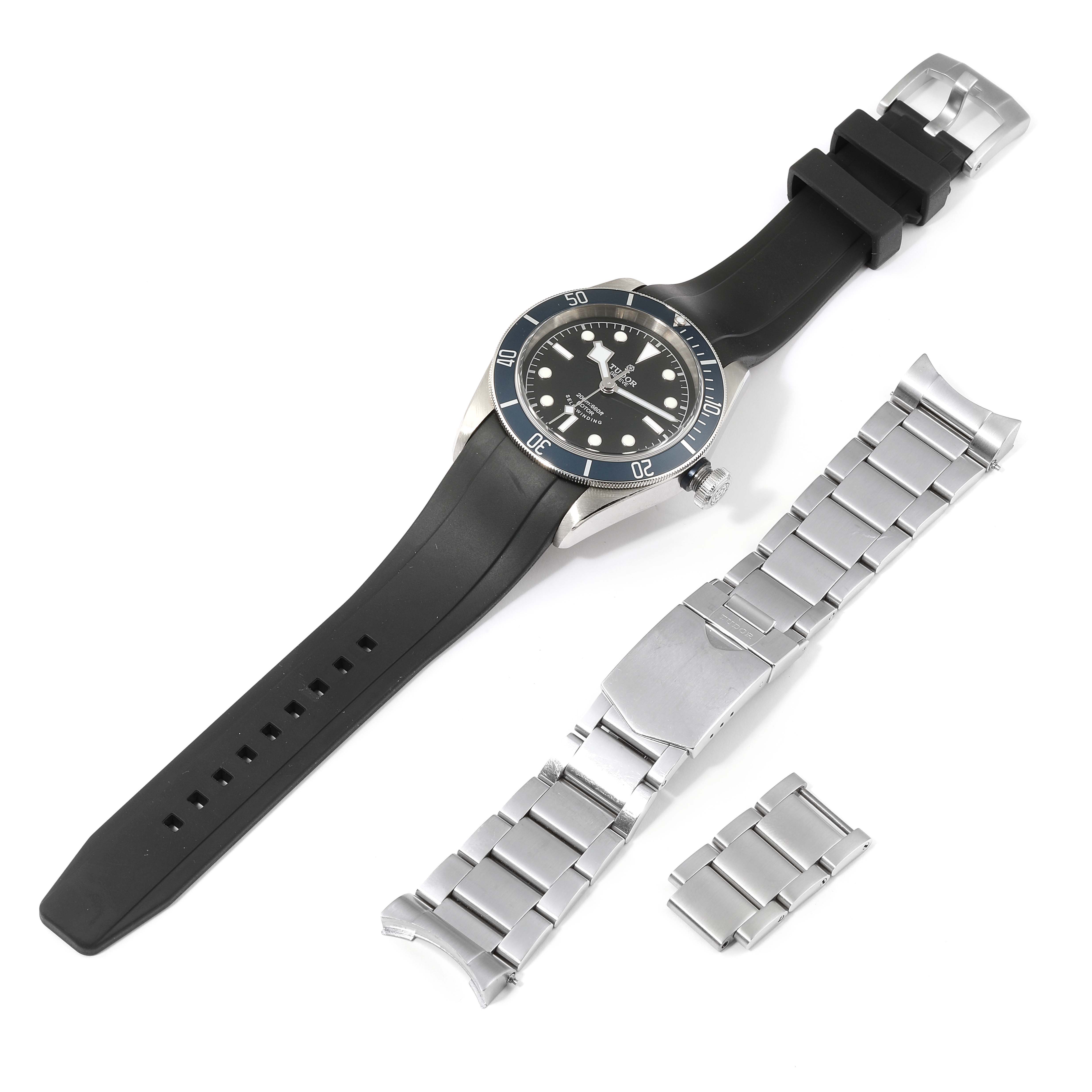 The image shows a Tudor Heritage Black Bay 79220 Men
s Stainless Steel Black Dial 79220 Men
s Stainless Steel Black Dial watch with a black strap, alongside a detached metal bracelet and extra links.