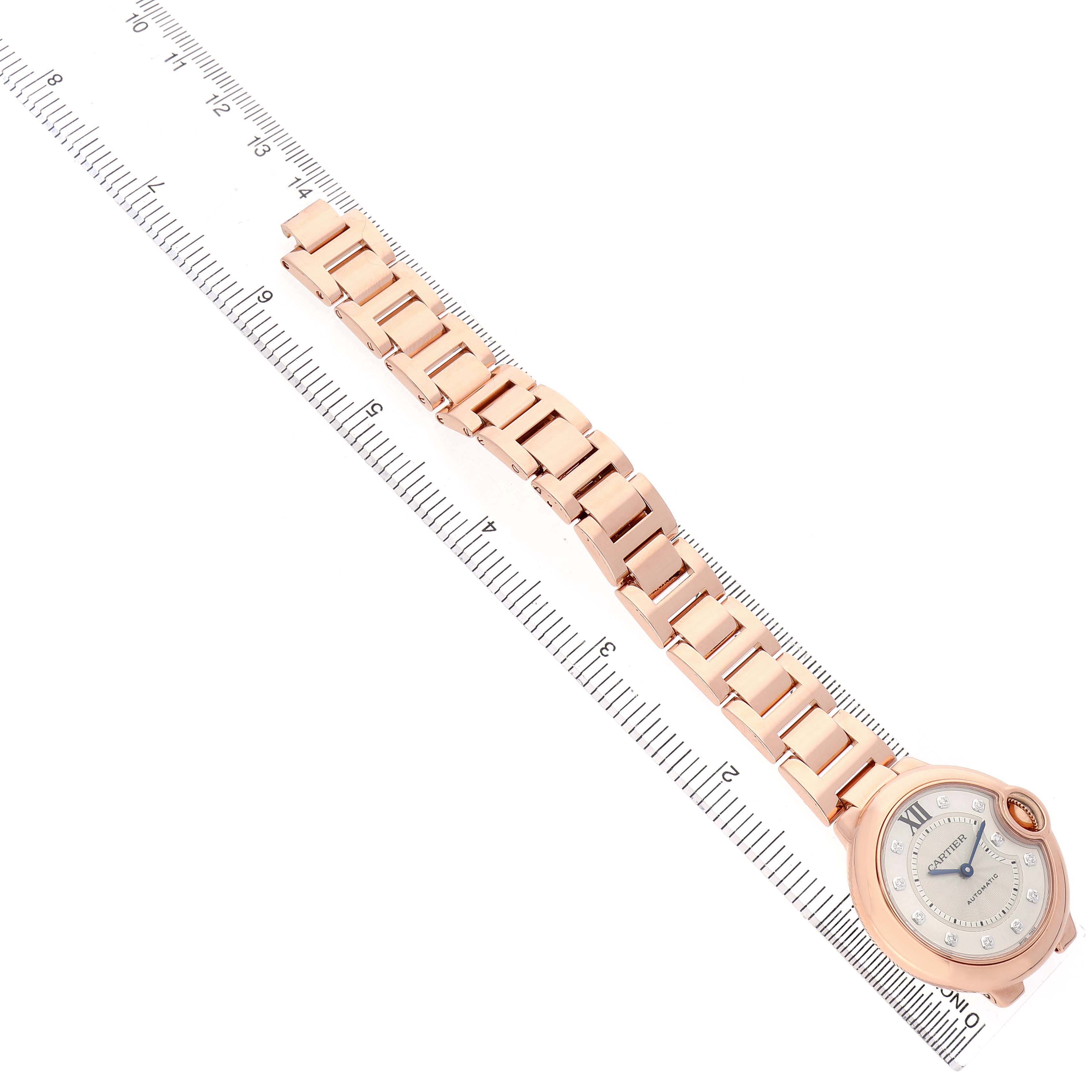 The Cartier Ballon Bleu WE902039 Women's Rose Gold Silver Dial watch is shown from a top-down angle, highlighting its face and metal bracelet along a ruler.