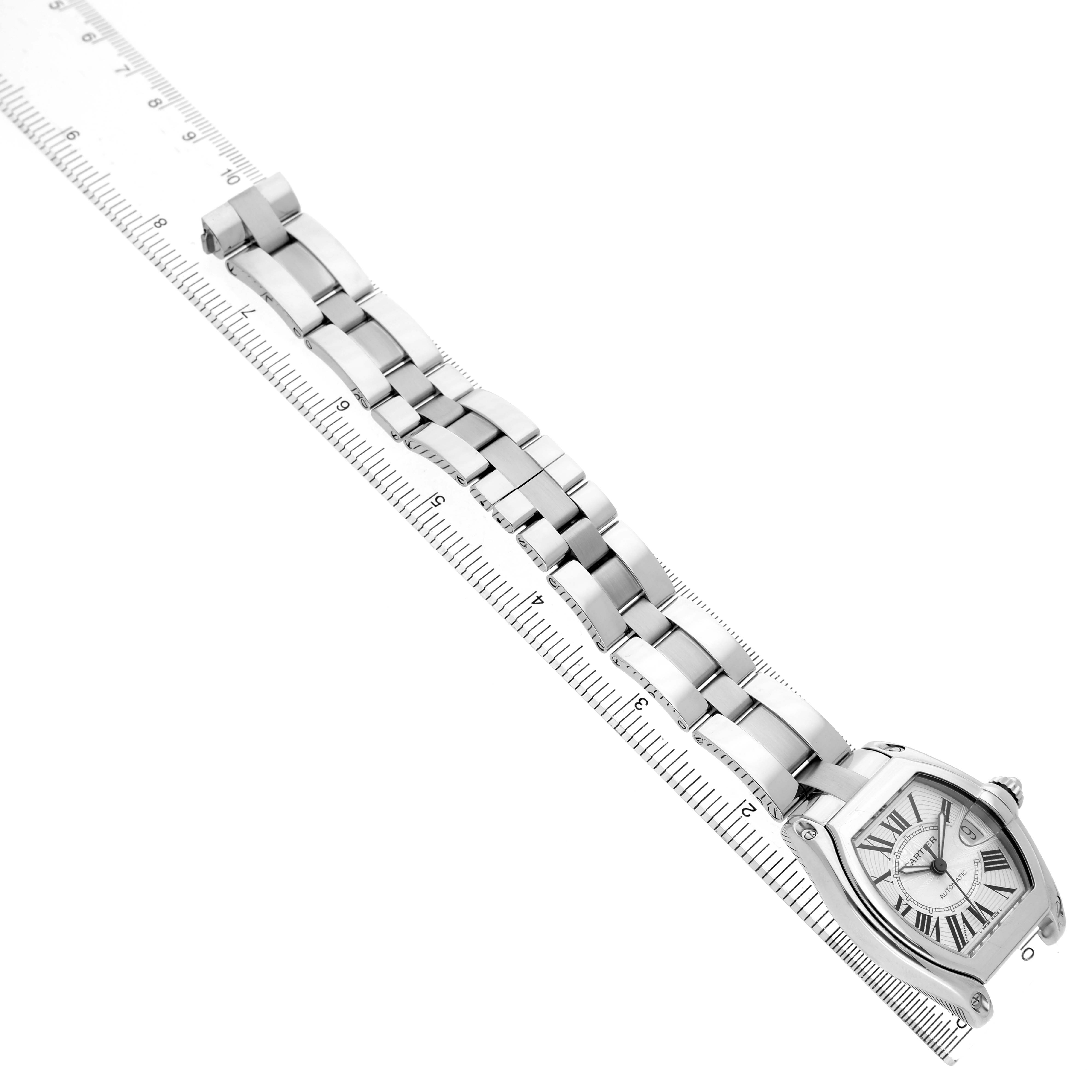 The Cartier Roadster W62025V3 Men's Stainless Steel Silver Dial watch is shown at an angle highlighting the face and bracelet, placed alongside a ruler for scale.