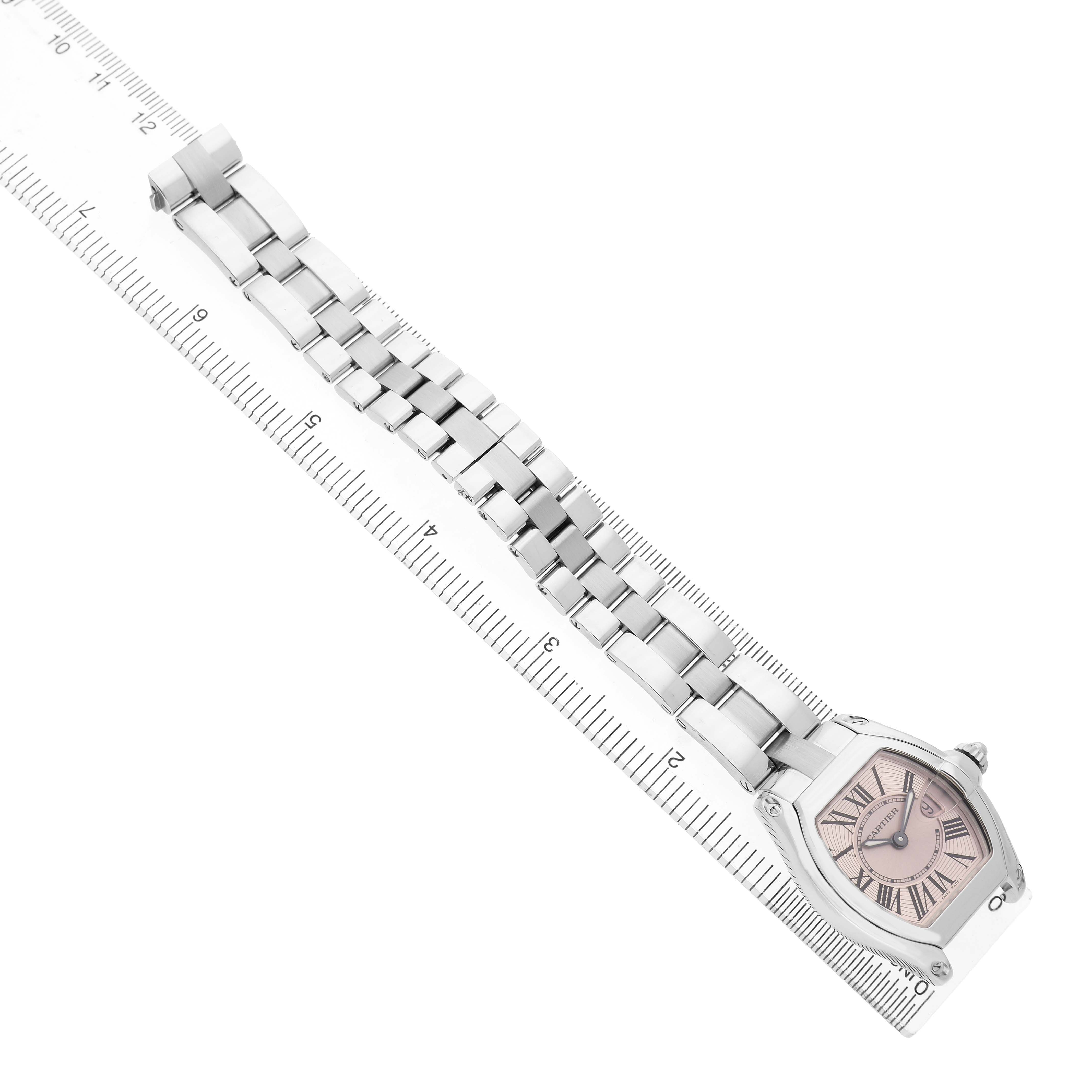 The Cartier Roadster W62017V3 Women's Stainless Steel Pink Dial model is shown laying flat with its case and metal bracelet visible, angled from the top-down alongside a ruler.