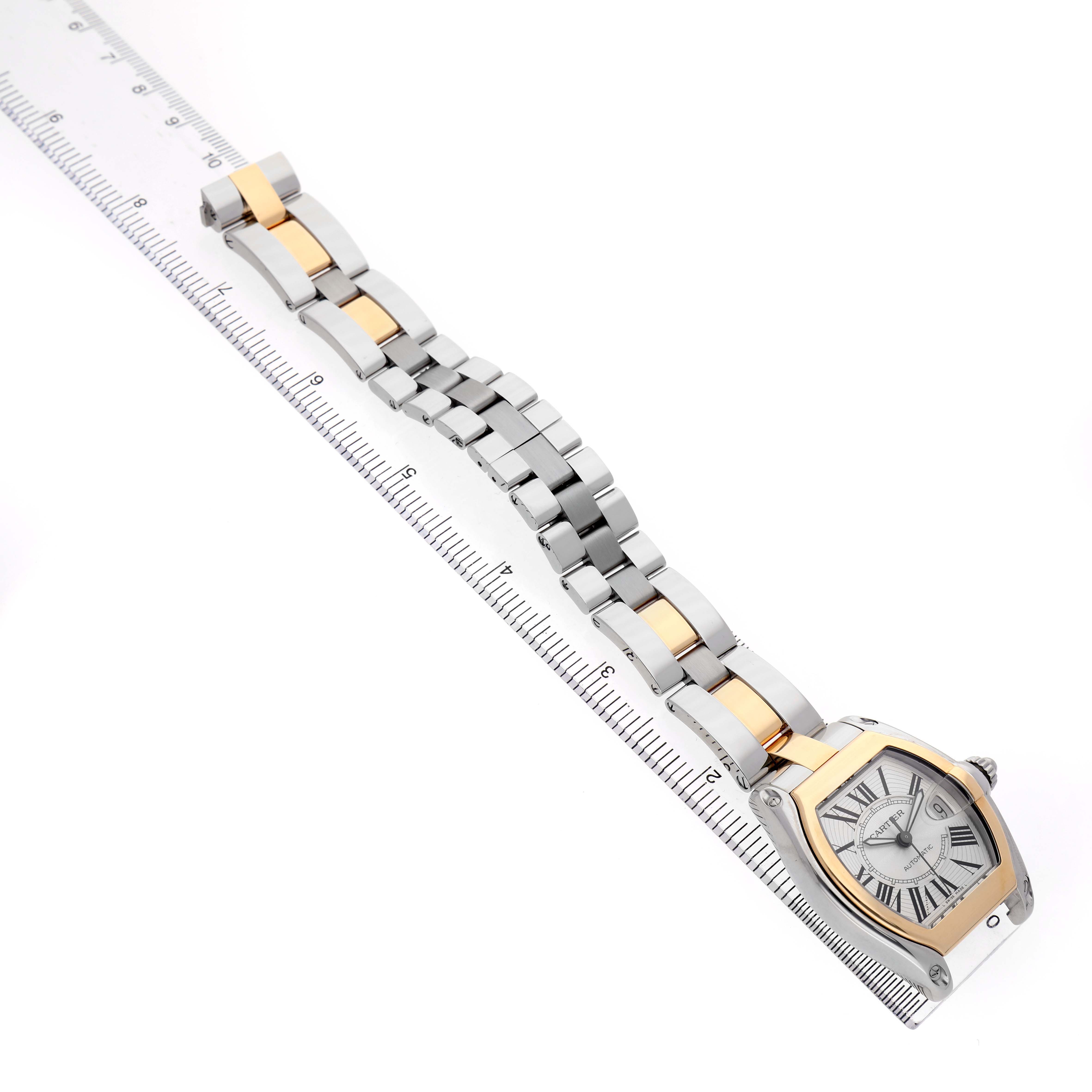 The Cartier Roadster W62031Y4 Men's Stainless Steel Silver Dial watch is shown diagonally, displaying its face, bracelet, and aligned with a measuring ruler.