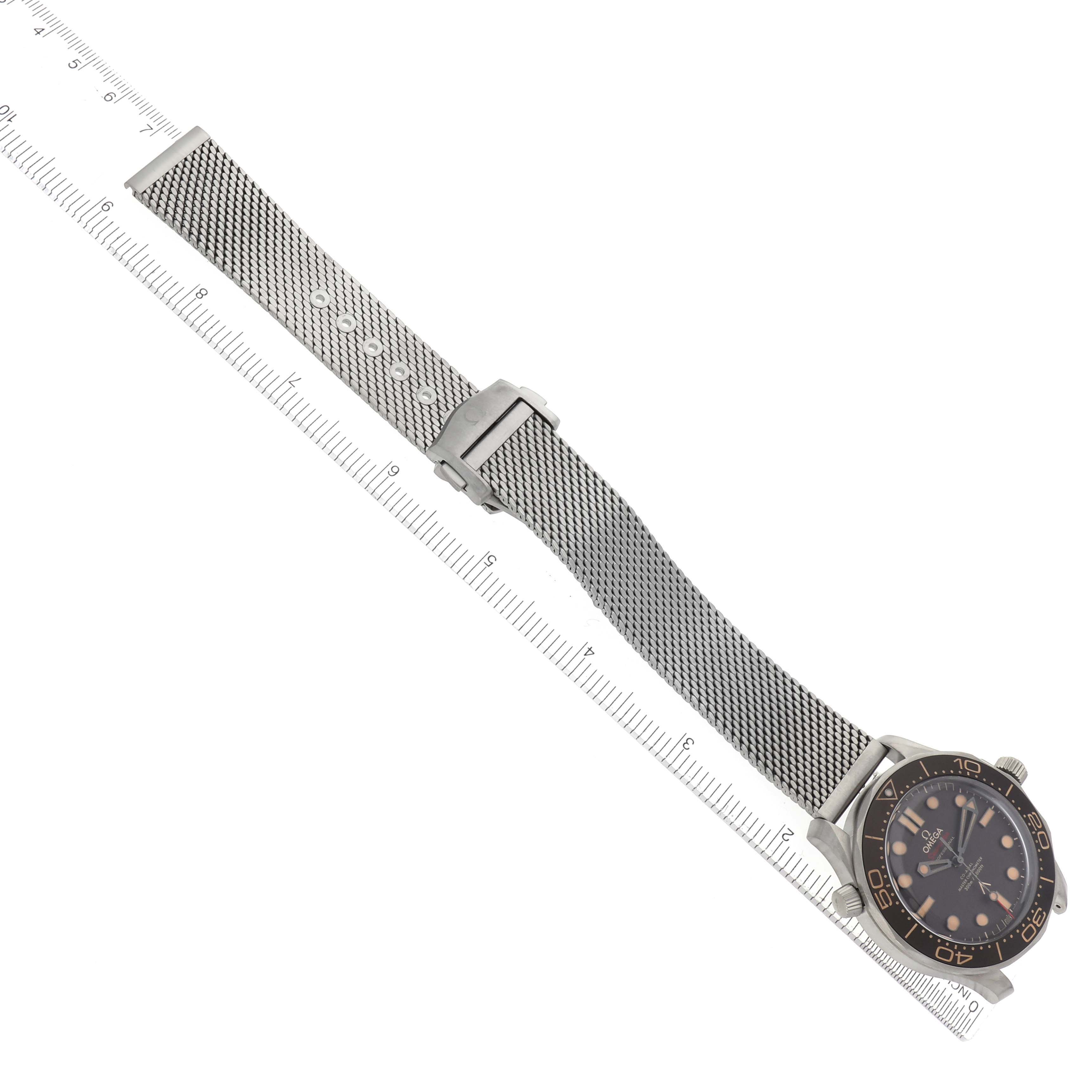 The image shows an angled view of the Omega Seamaster 210.90.42.20.01.001 Men
s Titanium Brown Dial watch with a mesh strap against a measuring ruler.