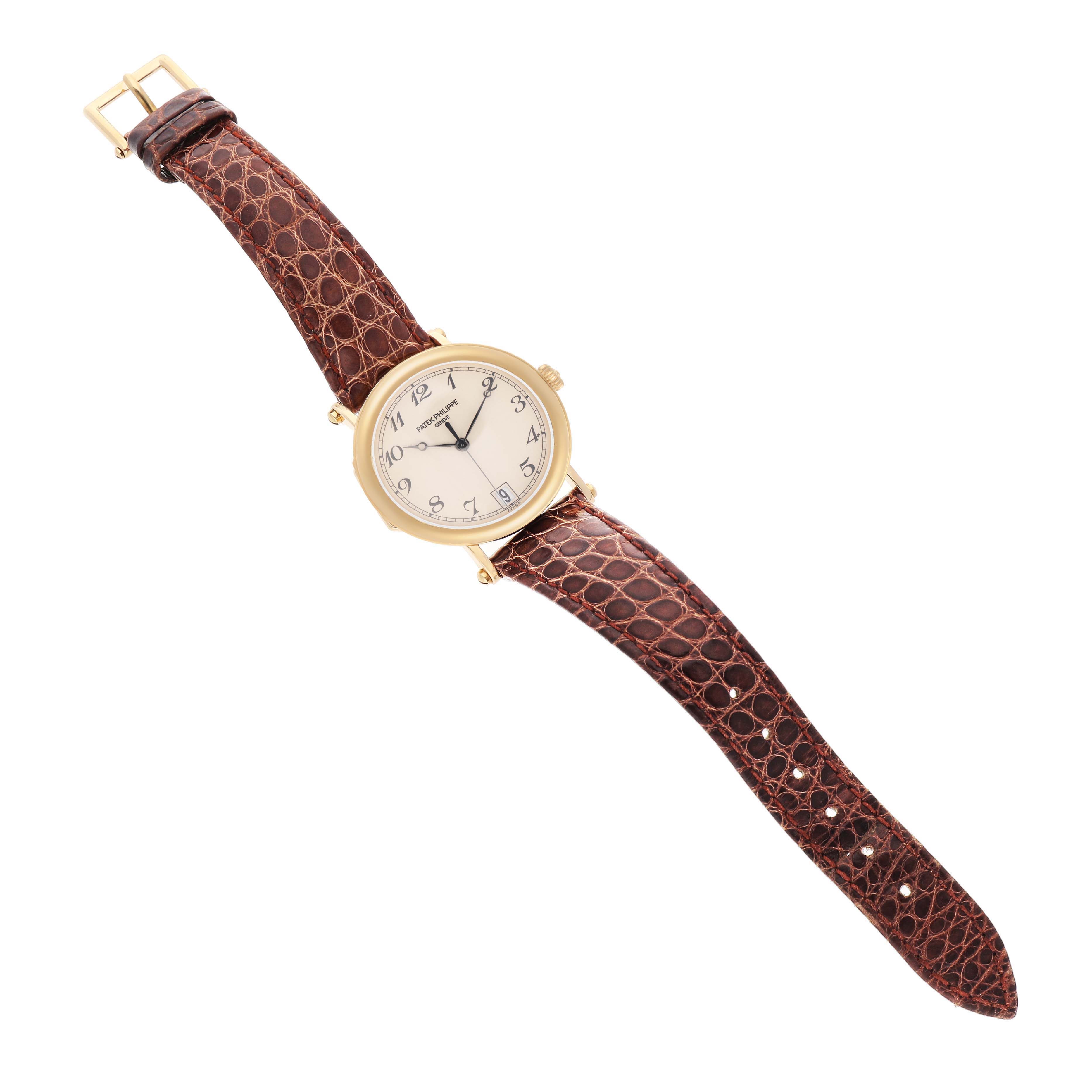 The Patek Philippe Calatrava 5053J Men's Yellow Gold White Dial watch is shown from a top-down angle, displaying the dial, leather strap, and gold case.