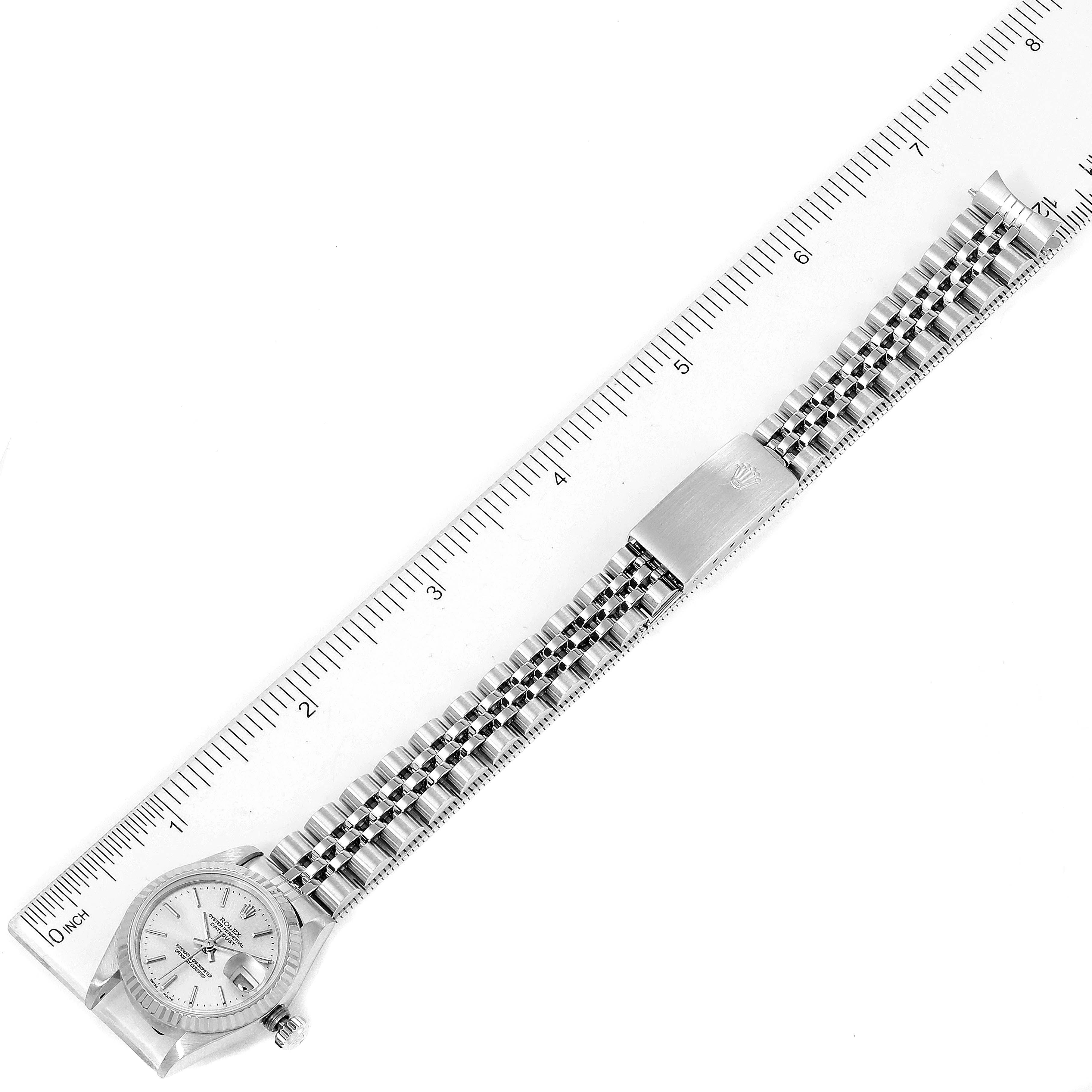 This image shows a Rolex Datejust 79174 Women
s Stainless Steel Silver Dial 79174 Women
s Stainless Steel Silver Dial watch laid flat with its bracelet fully extended, positioned alongside a ruler.