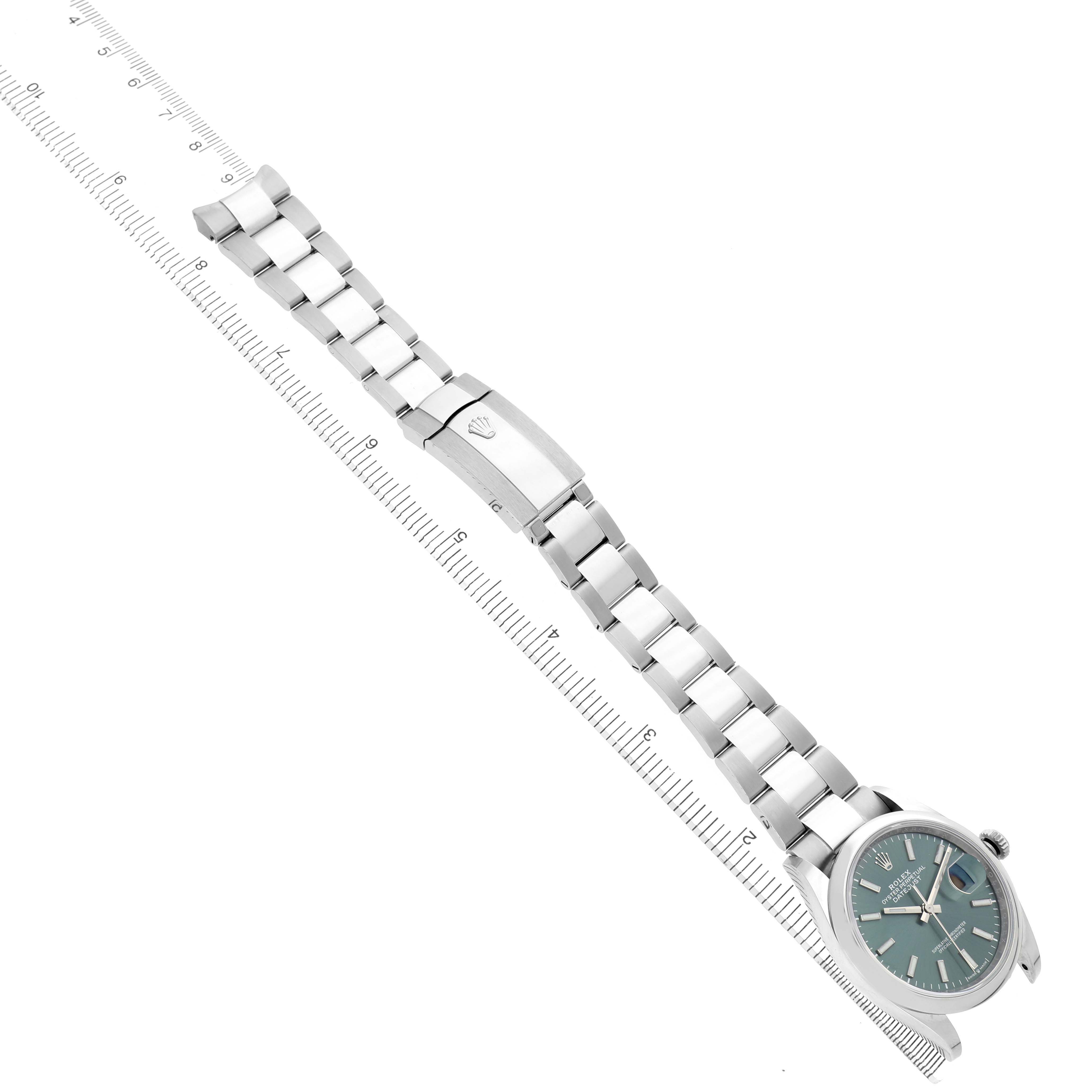 The Rolex Datejust 126200 Men's Stainless Steel Green Dial watch is shown from a top angle, highlighting the face, bracelet, and clasp with a measurement ruler beside it.