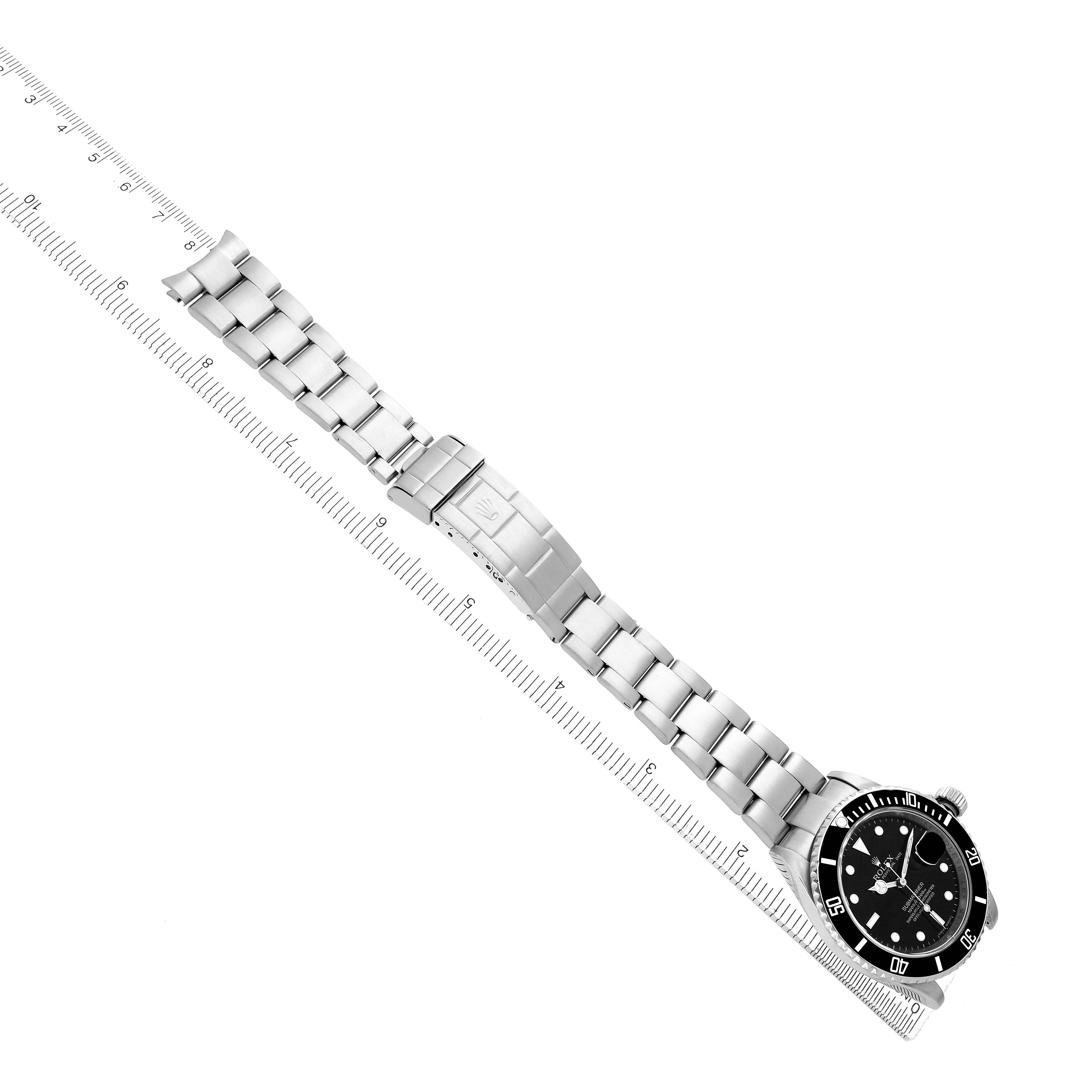 The Rolex Submariner 16610 Men
s Stainless Steel Black Dial watch is shown from an angled top-down view, displaying the bracelet, clasp, and face with a ruler beside it.