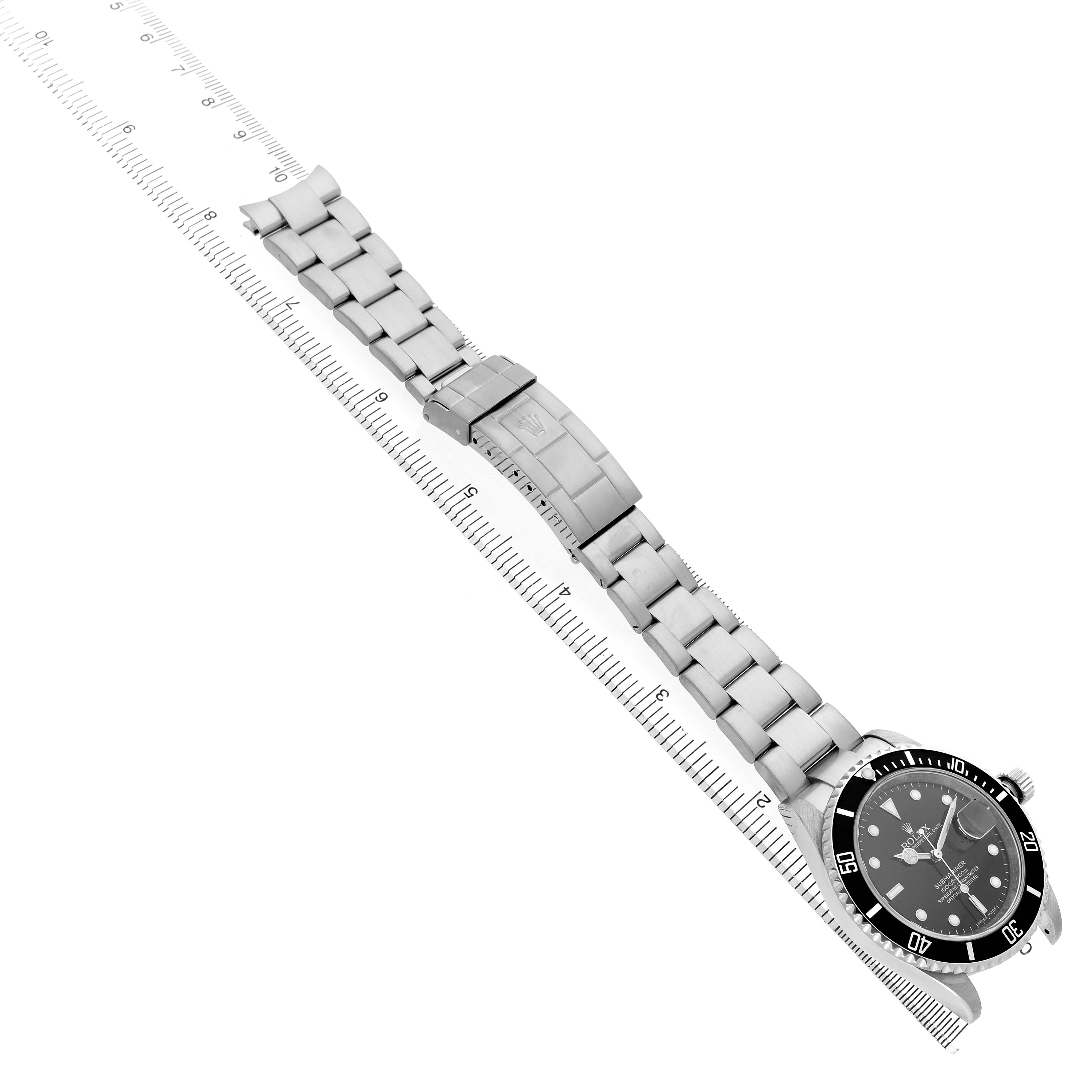 The Rolex Submariner 16610 Men's Stainless Steel Black Dial watch is shown from the top, displaying the bracelet, clasp, and face with a ruler beside it.