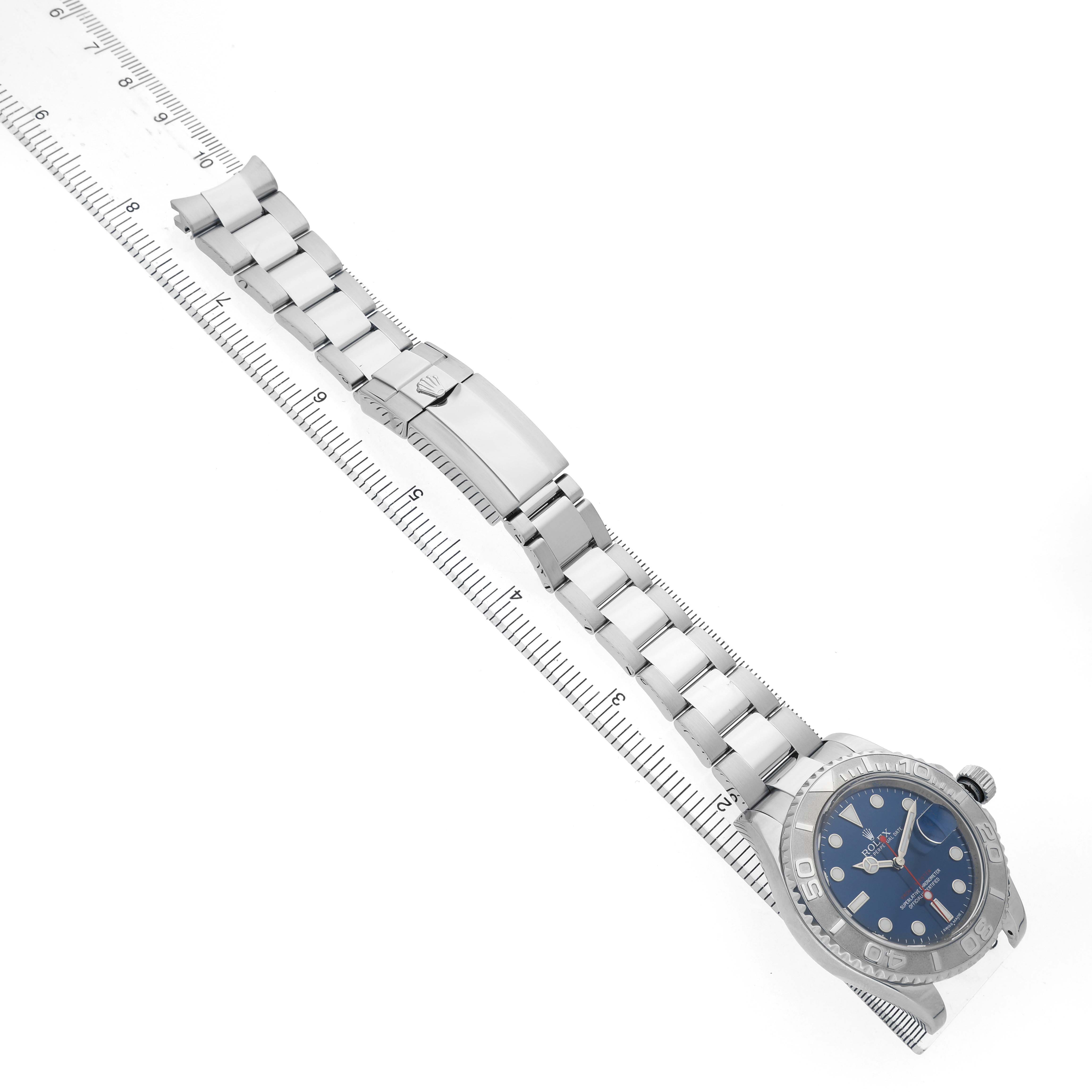 The Rolex Yacht-Master 116622 Men's Stainless Steel Blue Dial watch is shown from a top-down angle, displaying the face, bezel, bracelet, and clasp on a ruler.