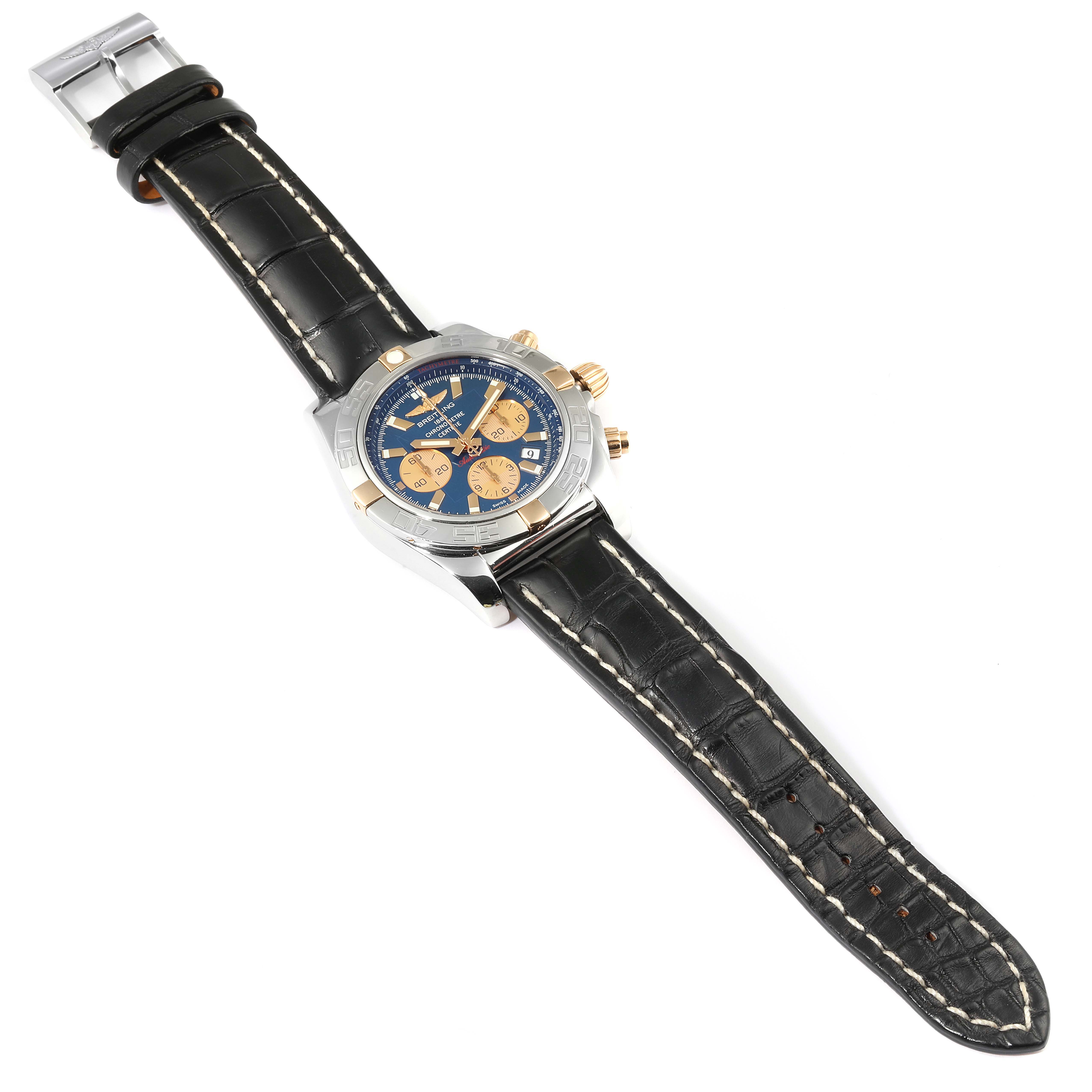 This image shows a Breitling Chronomat IB0110 Men's Steel and Gold (two tone) Blue Dial IB0110 Men's Steel and Gold (two tone) Blue Dial watch laid flat, displaying its black leather strap, blue and gold dial, and side pushers.