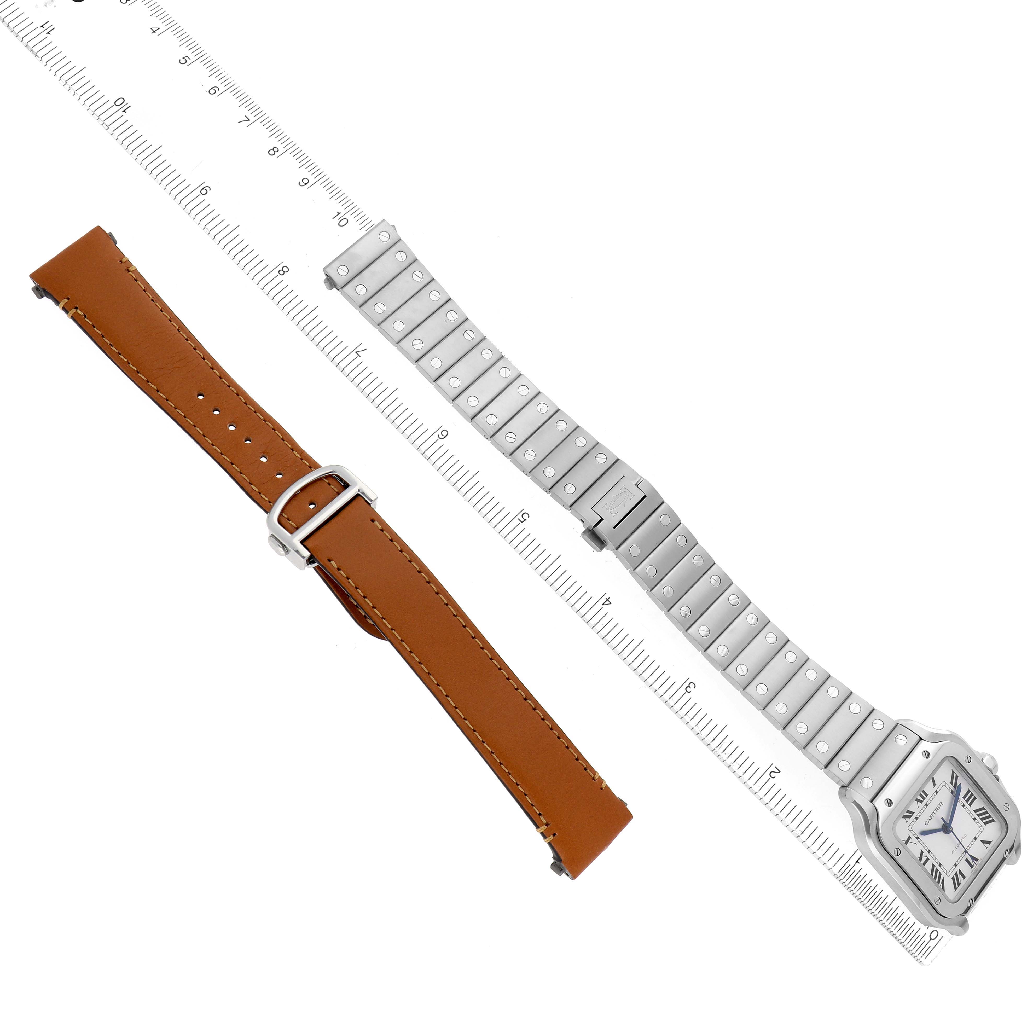 The image shows a Cartier Santos WSSA0029 Men
s Stainless Steel Silver Dial watch with a metal bracelet and a separate brown leather strap laid flat alongside a ruler.