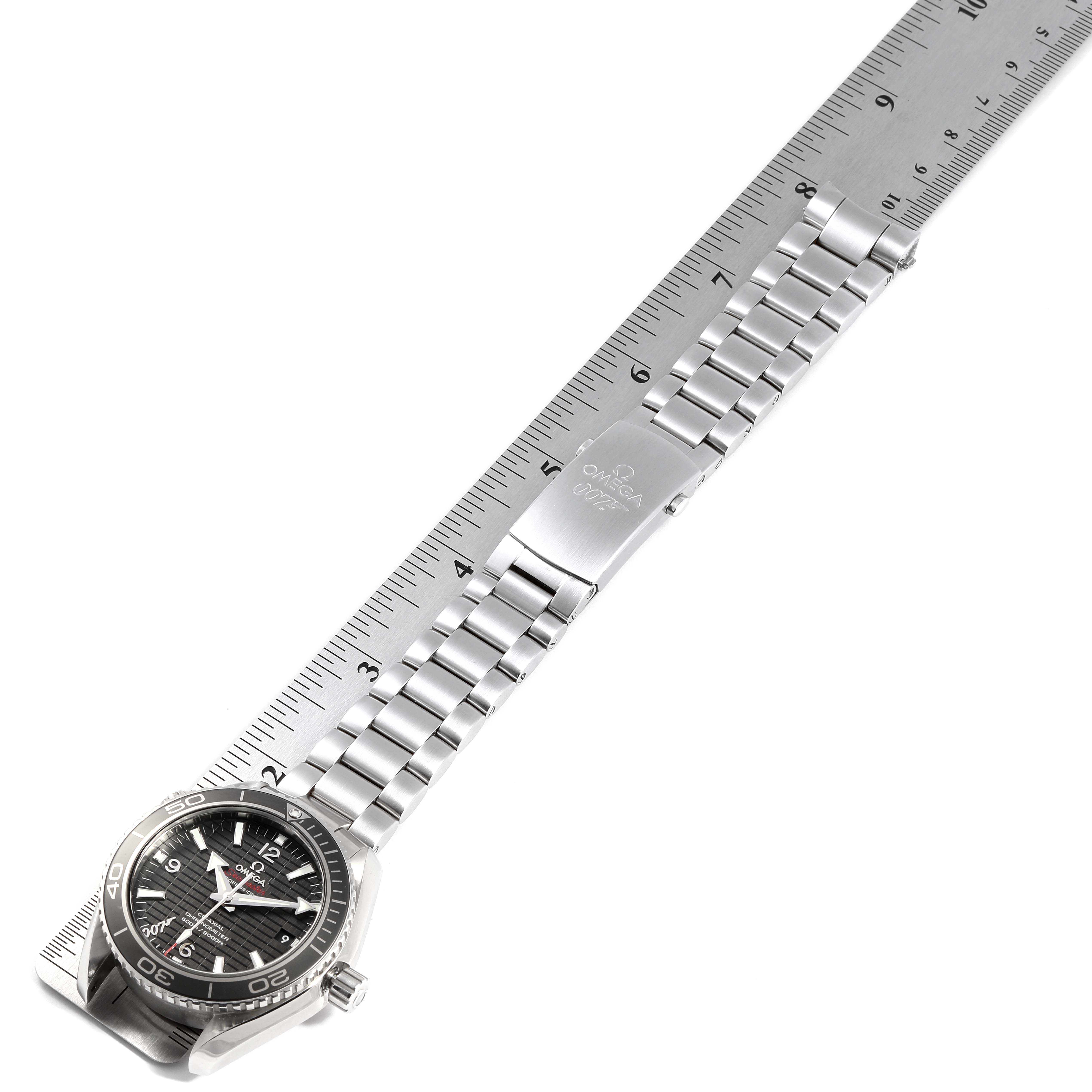 The image shows an Omega Planet Ocean 232.30.42.21.01.004 Men's Stainless Steel Black Dial 232.30.42.21.01.004 Men's Stainless Steel Black Dial watch at an angle with its stainless steel bracelet stretched out, placed alongside a ruler.