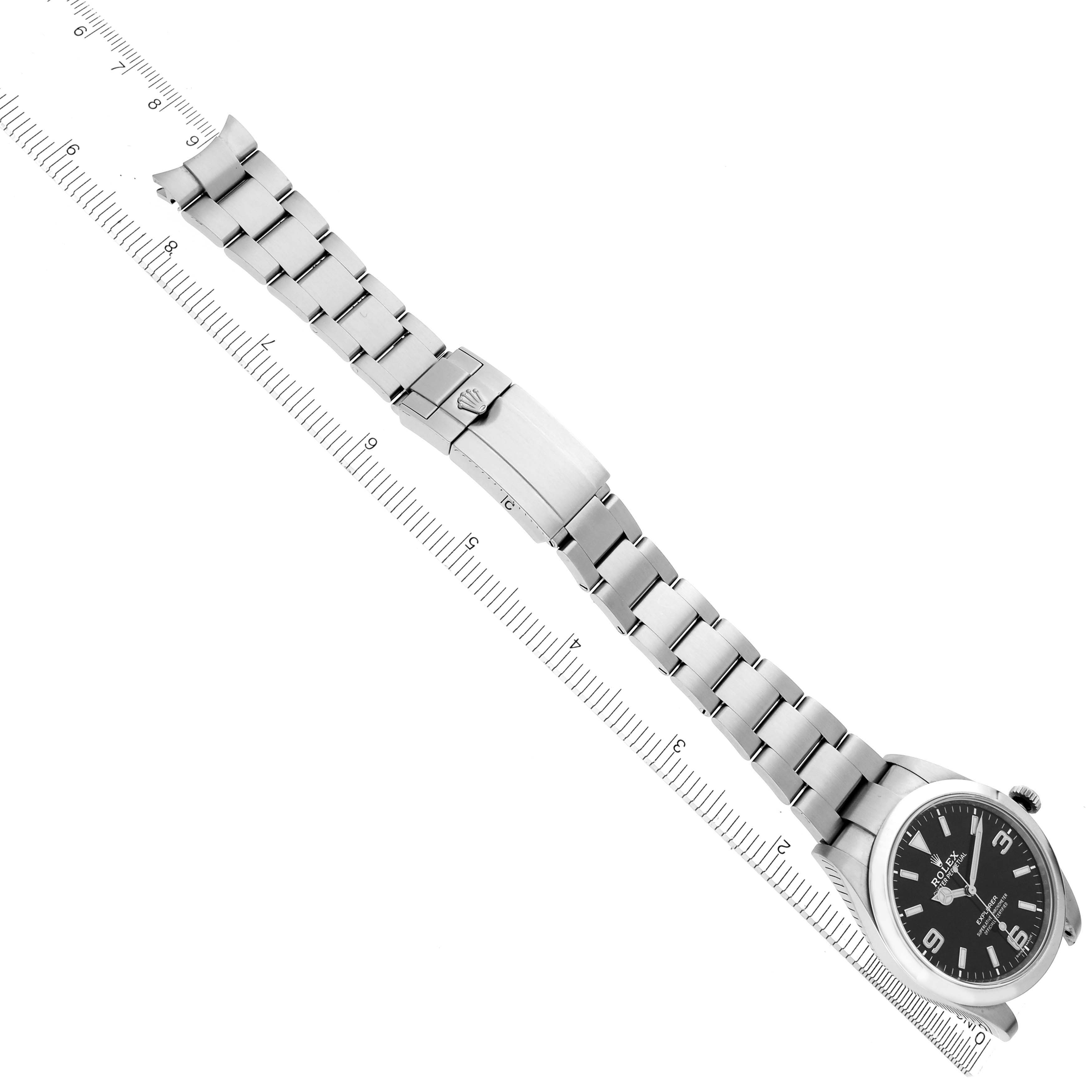 The Rolex Explorer 214270 Men's Stainless Steel Black Dial watch is shown from a top-down angle, highlighting the band, clasp, and watch face alongside a ruler.