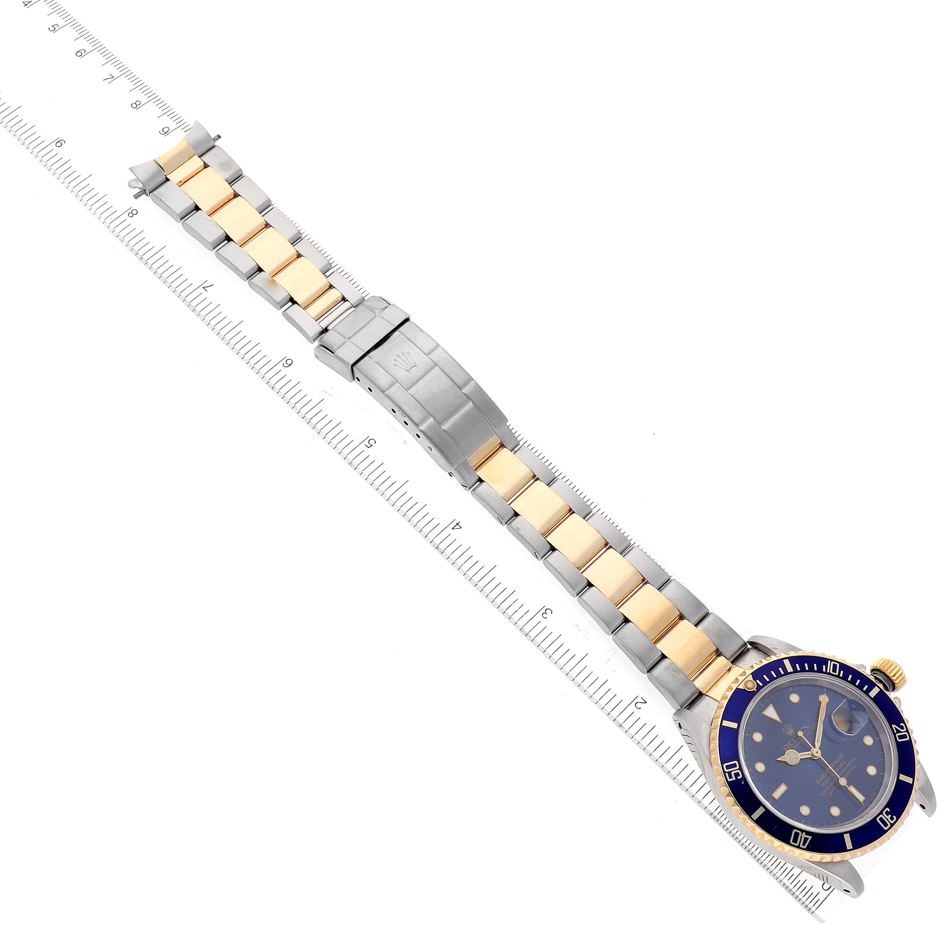 The image shows a Rolex Submariner 16613 Men's Steel and Gold (two tone) Blue Dial 16613 Men's Steel and Gold (two tone) Blue Dial watch laid flat with its gold and silver bracelet fully extended alongside a ruler for scale.