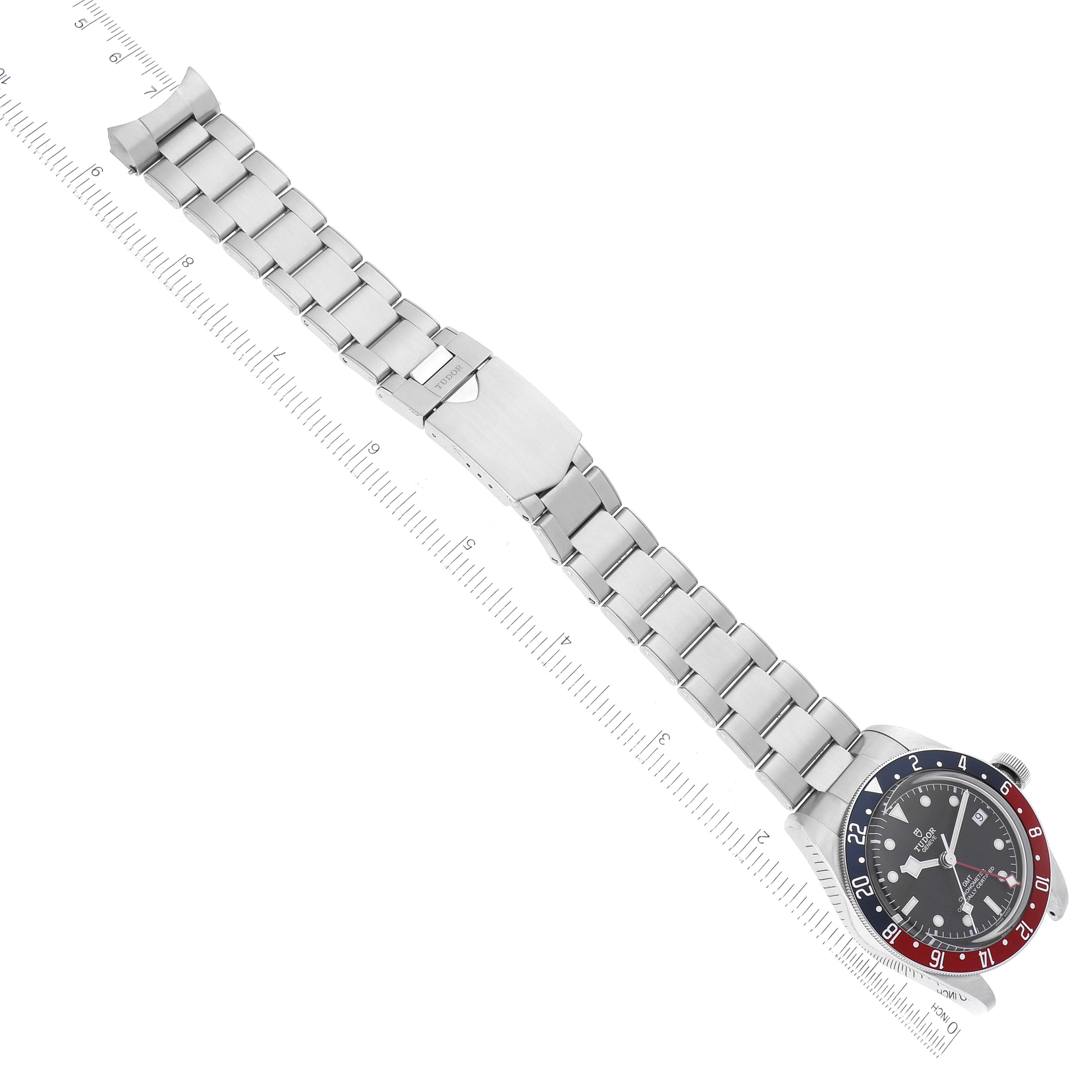 This image shows the Tudor Heritage Black Bay 79830RB Men's Stainless Steel Black Dial 79830RB Men's Stainless Steel Black Dial watch from an angled top-down view, highlighting the dial, bezel, and bracelet with a ruler beside it.