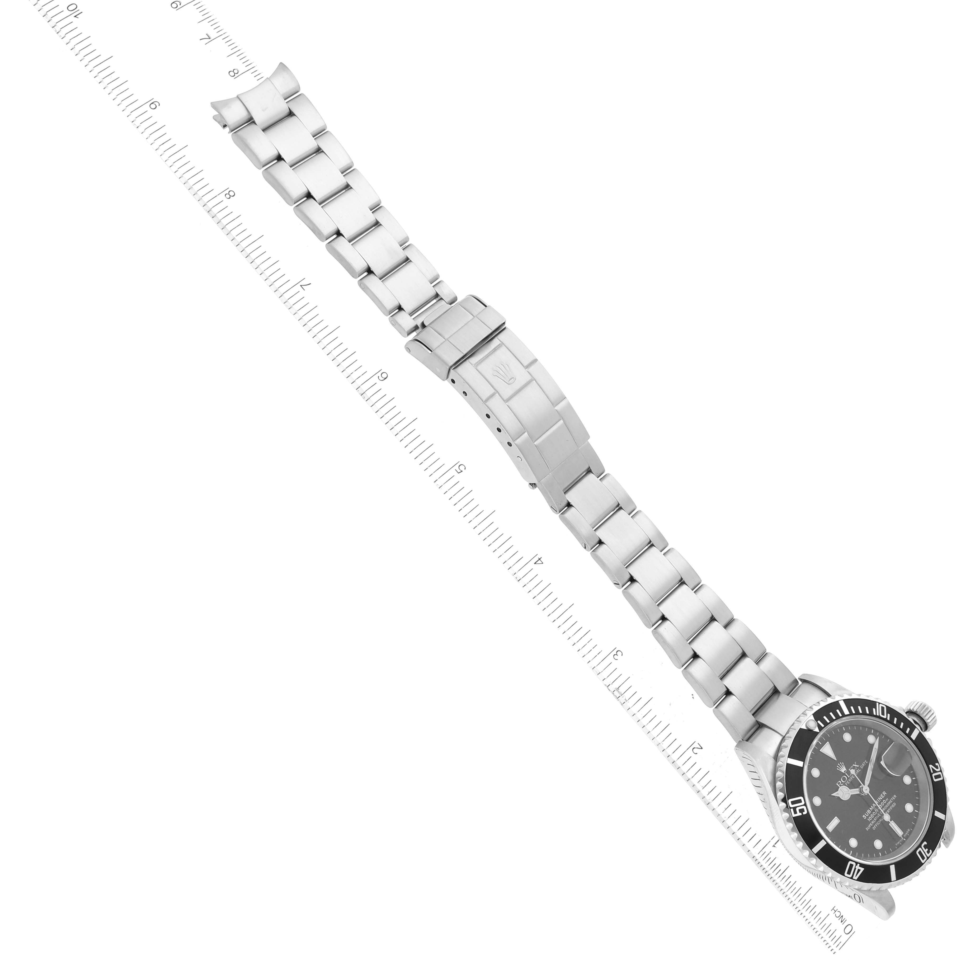This image shows a top-down angle of a Rolex Submariner 16610 Men
s Stainless Steel Black Dial 16610 Men
s Stainless Steel Black Dial, highlighting the watch face, bracelet, and clasp laid next to a ruler.
