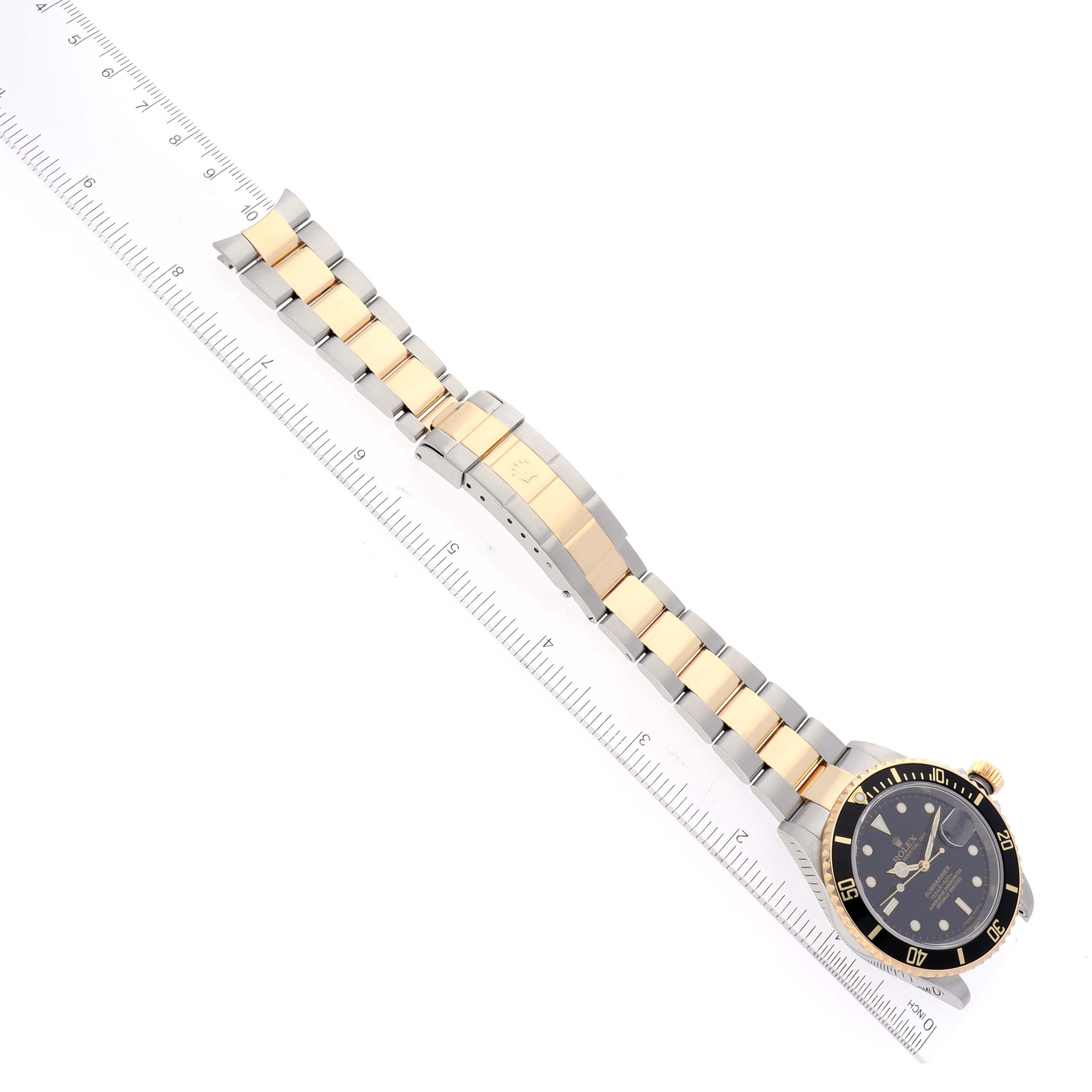 This image shows a top view of a Rolex Submariner 16613 Men's Steel and Gold (two tone) Black Dial 16613 Men's Steel and Gold (two tone) Black Dial watch with a two-tone bracelet next to a ruler.