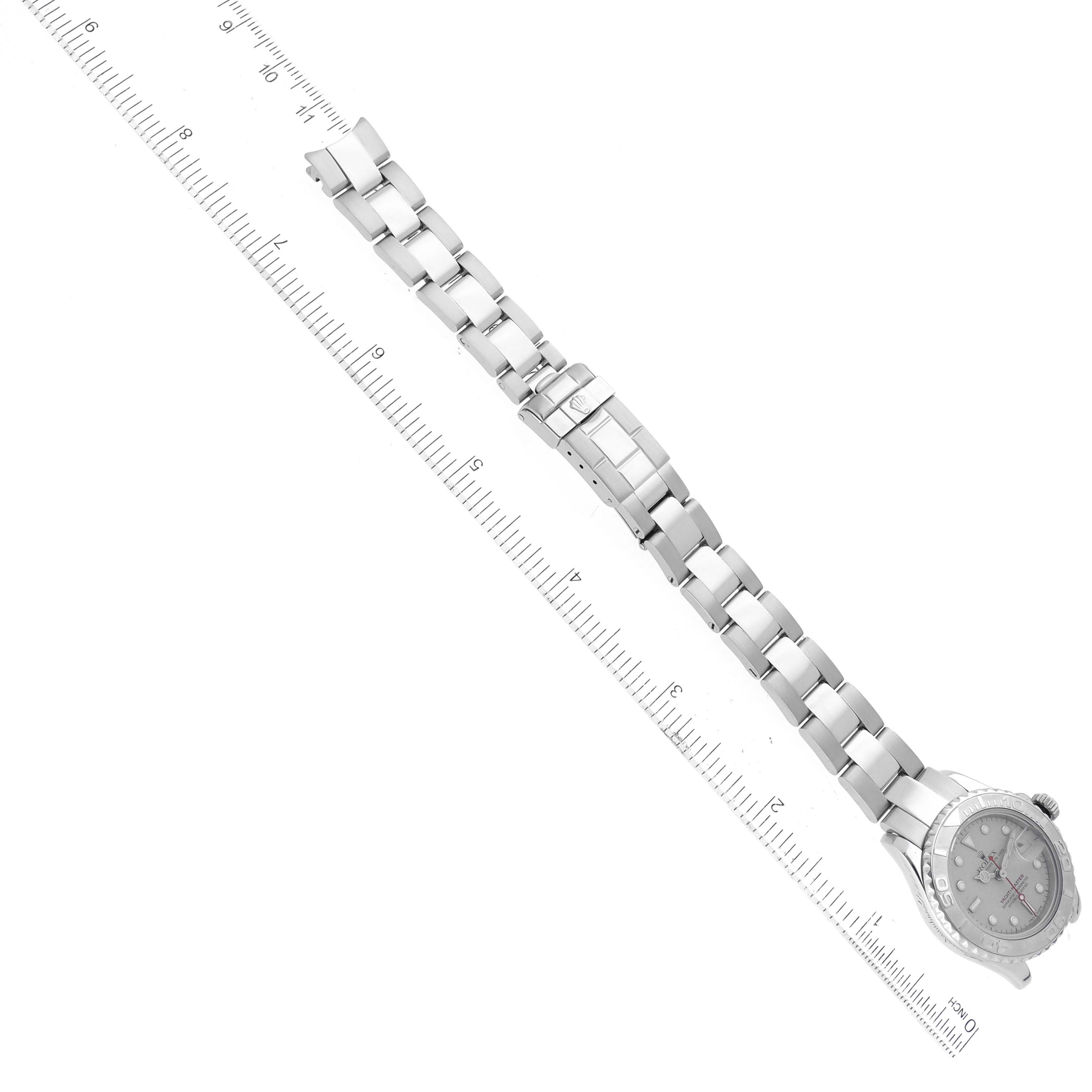 The image shows a top view of a Rolex Yacht-Master 169622 Women
s Stainless Steel Silver Dial 169622 Women
s Stainless Steel Silver Dial watch and its metal bracelet, aligned with a ruler for scale.