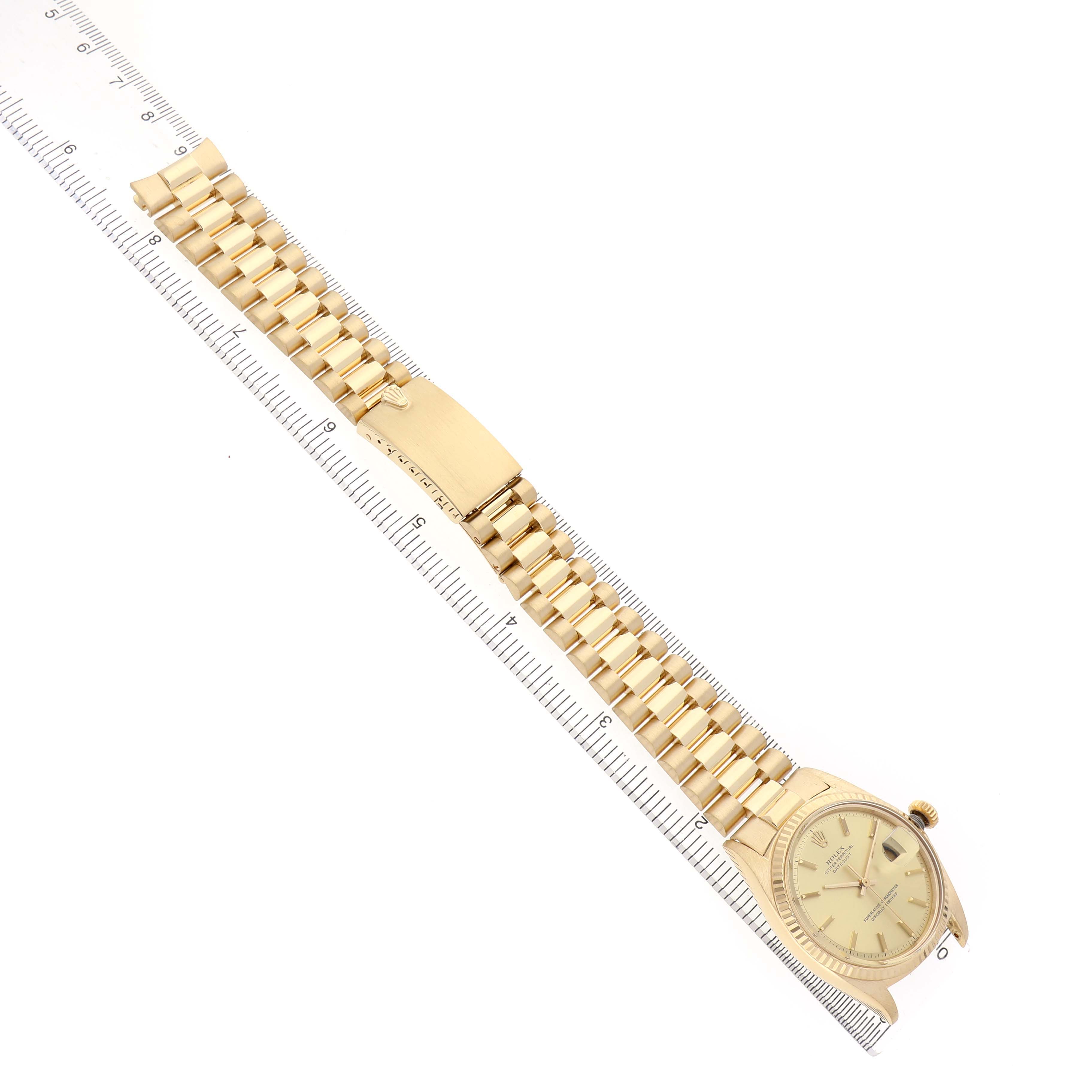 The Rolex Vintage Collection 1601 Men's Yellow Gold Champagne Dial watch is shown diagonally, featuring its gold bracelet, clasp, and dial, aligned alongside a ruler.
