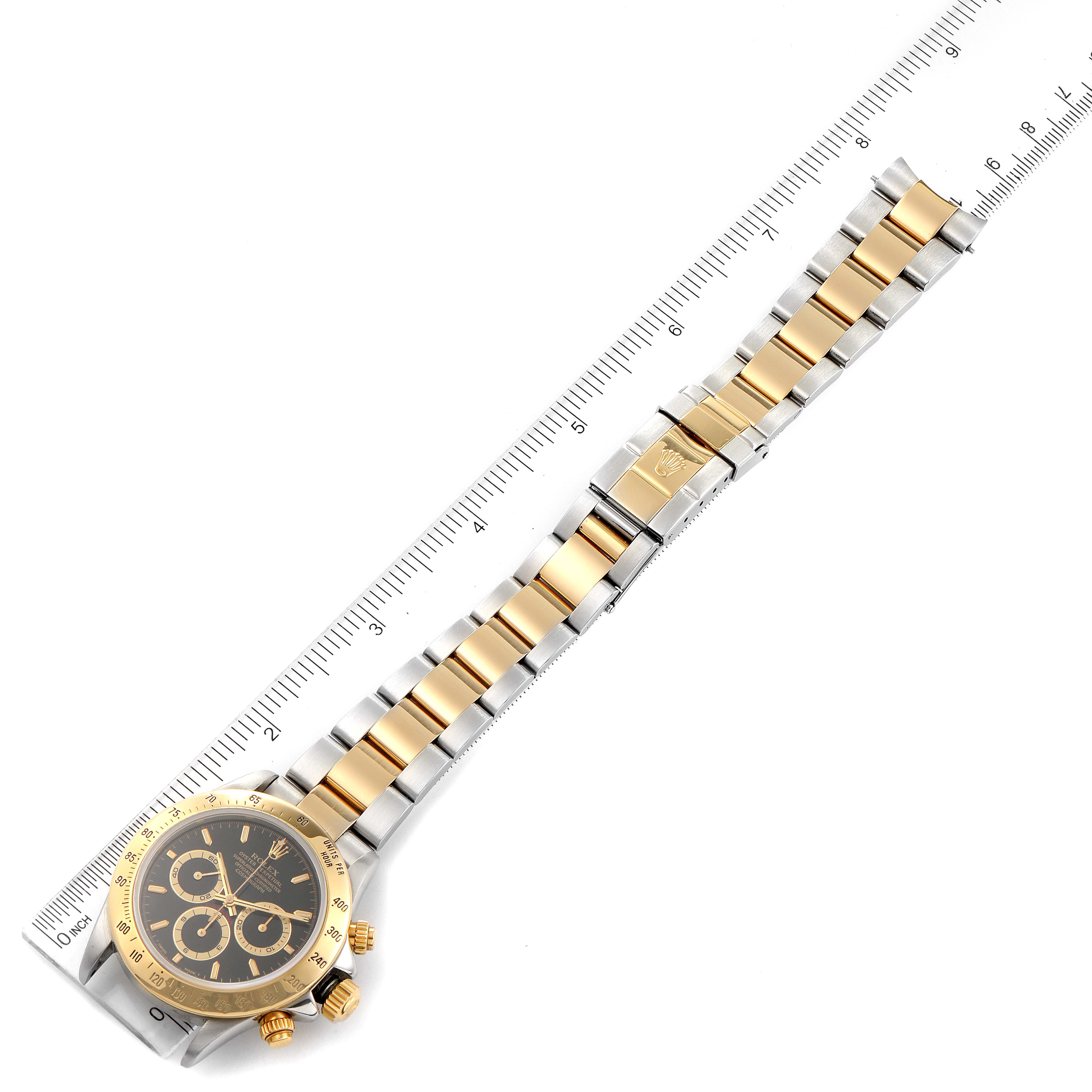The image shows a Rolex Daytona 16523 Men
s Steel and Gold (two tone) Black Dial 16523 Men
s Steel and Gold (two tone) Black Dial watch, featuring its dial, bezel, and bracelet, all aligned with a ruler.