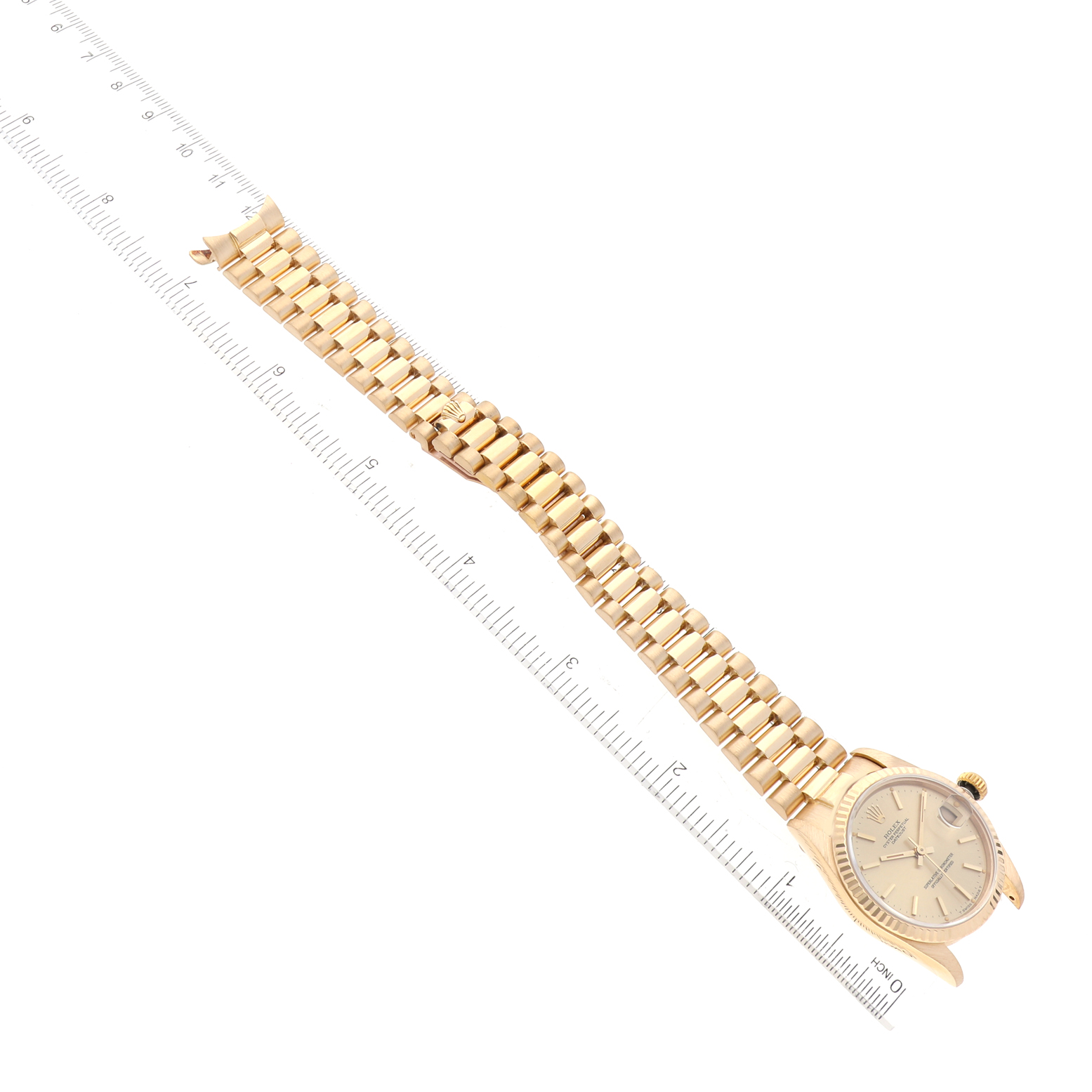 This image shows the Rolex President 68278 Women's Yellow Gold Champagne Dial 68278 Women's Yellow Gold Champagne Dial model watch laying flat with its bracelet extended, alongside a measuring ruler.