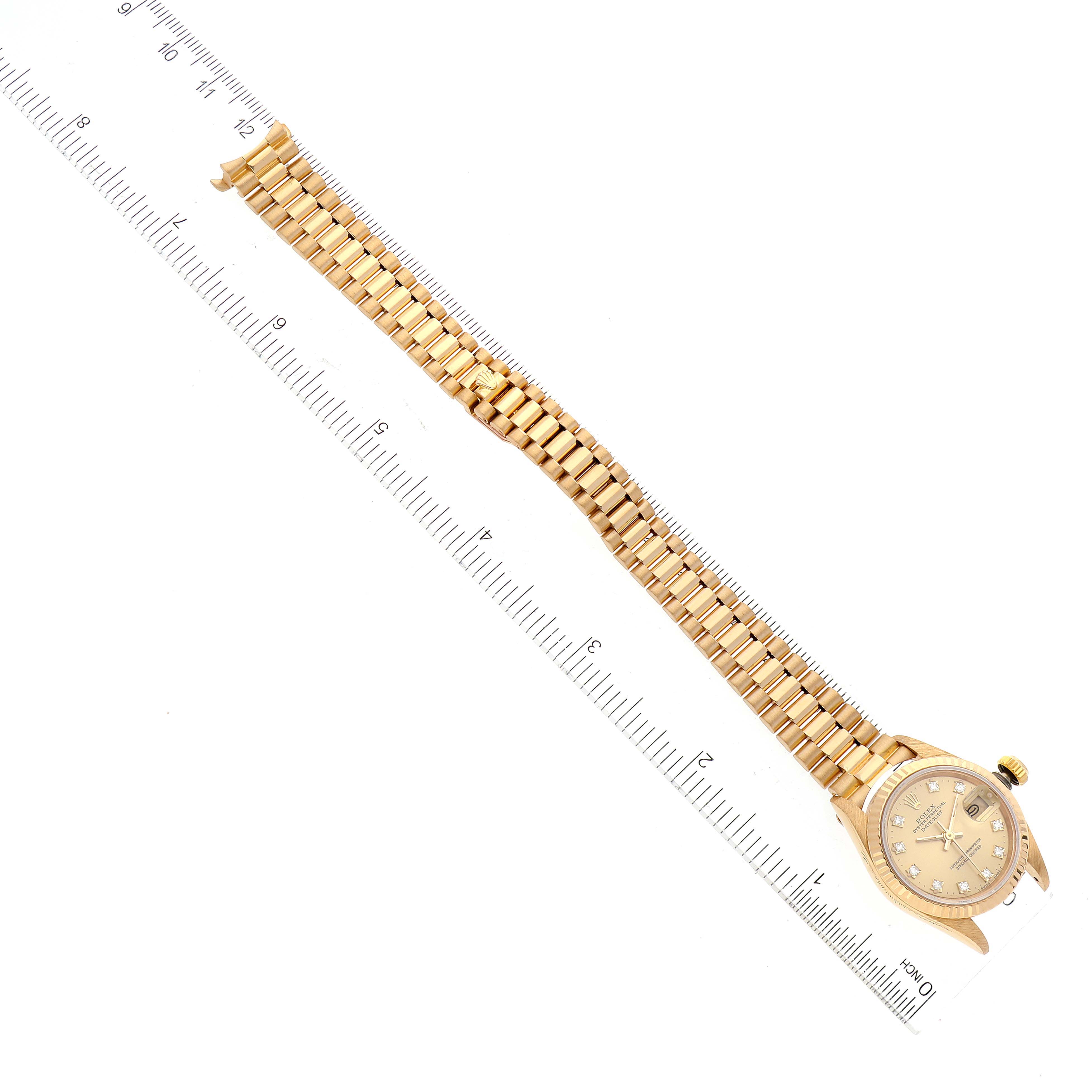 The image shows a Rolex President 69178 Women
s Yellow Gold Champagne Dial 69178 Women
s Yellow Gold Champagne Dial model watch at a flat angle with a detailed view of its gold bracelet and face alongside a ruler.